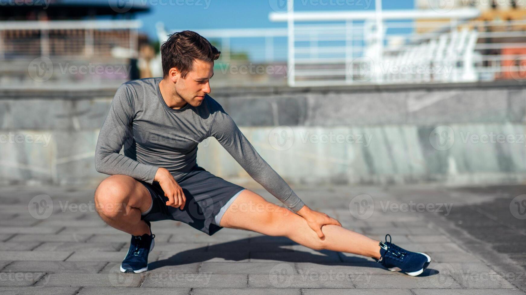 Athletic body and healthy lifestyle. Millennial man in sportswear squat and doing leg exercises on street, panorama, free space photo