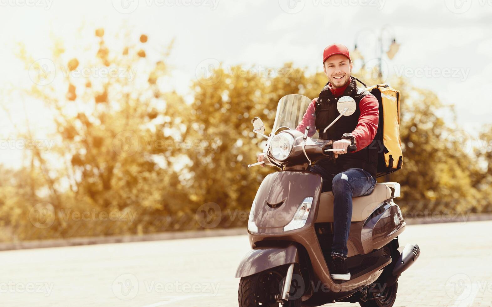 Courier Delivering Food In Yellow Backpack Riding Motorbike Outside In City. Meal Delivering Service. Copy Space photo