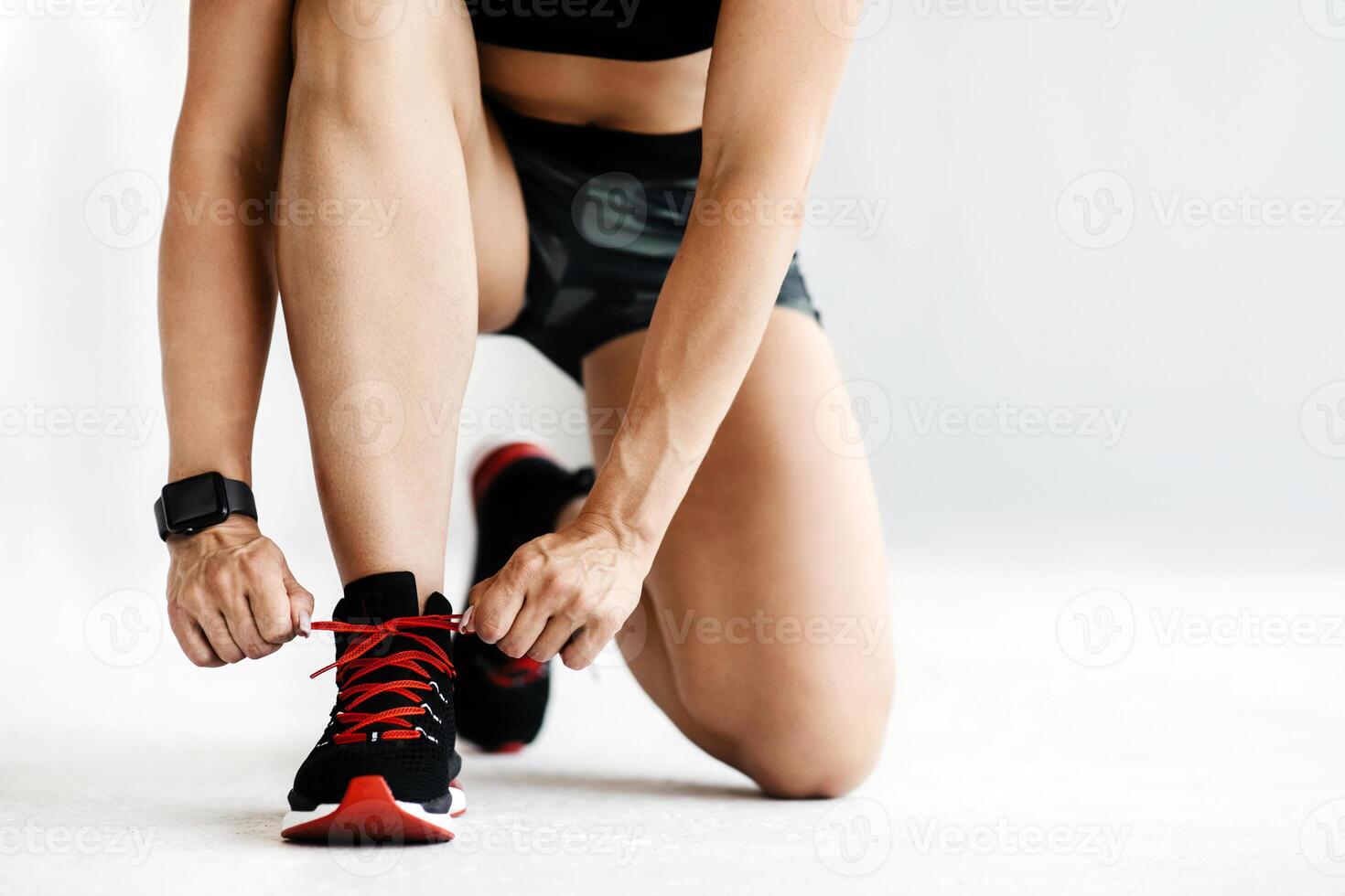 Start of training and modern sports at home or gym. Adult strong female in sports uniform and fitness tracker ties shoelaces in morning during covid-19 quarantine, indoor, cropped, studio shot photo