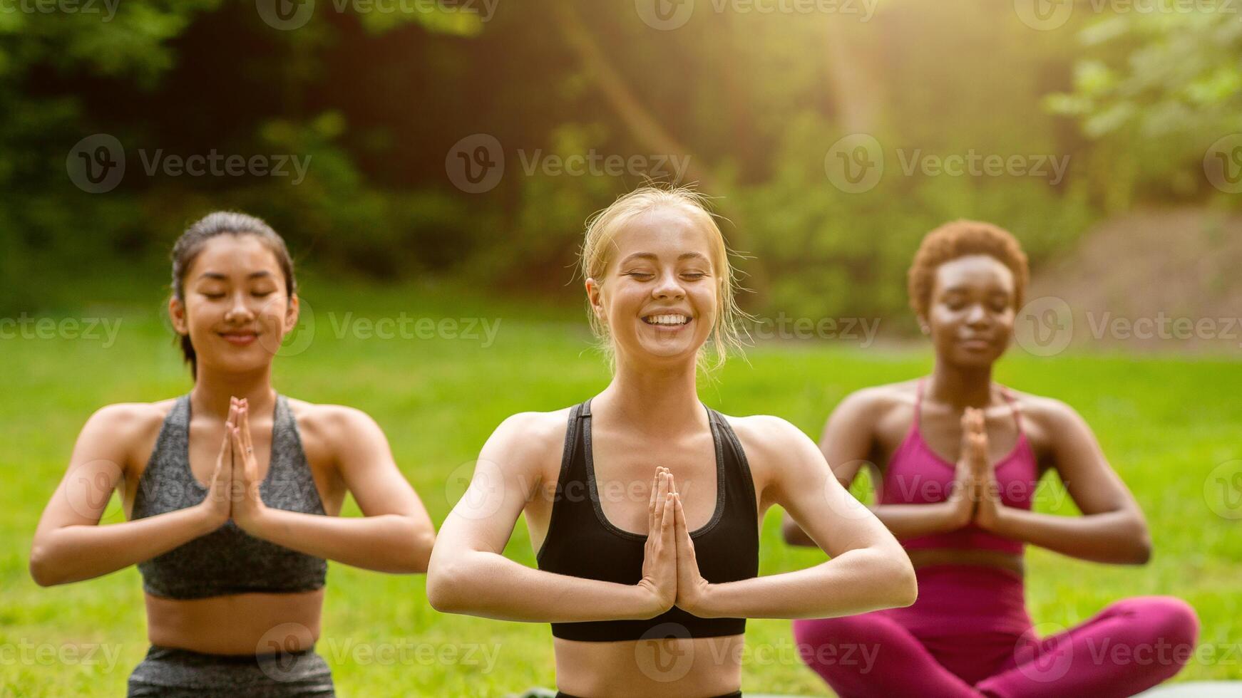 Happy multiethnic women meditating during their morning yoga practice at park, copy space photo