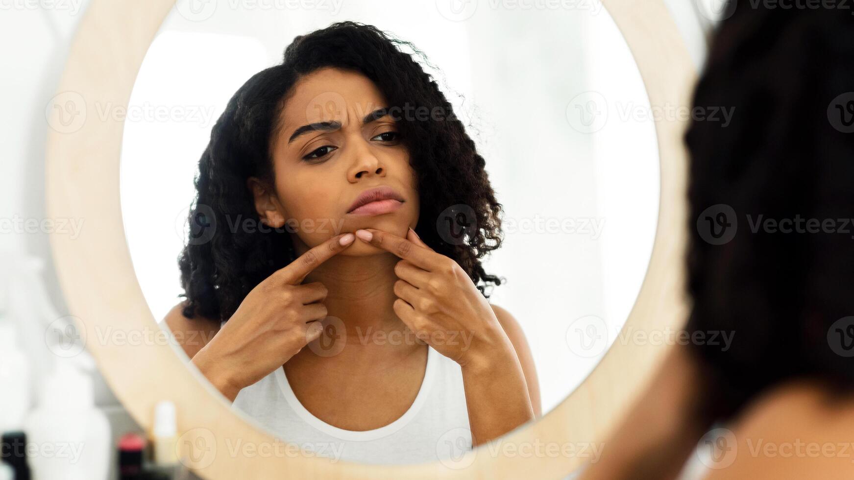 Problem Skin Concept. African American Girl Looking In Mirror and Touching Pimple, Worry About Acne, Over Shoulder View, Selective Focus photo