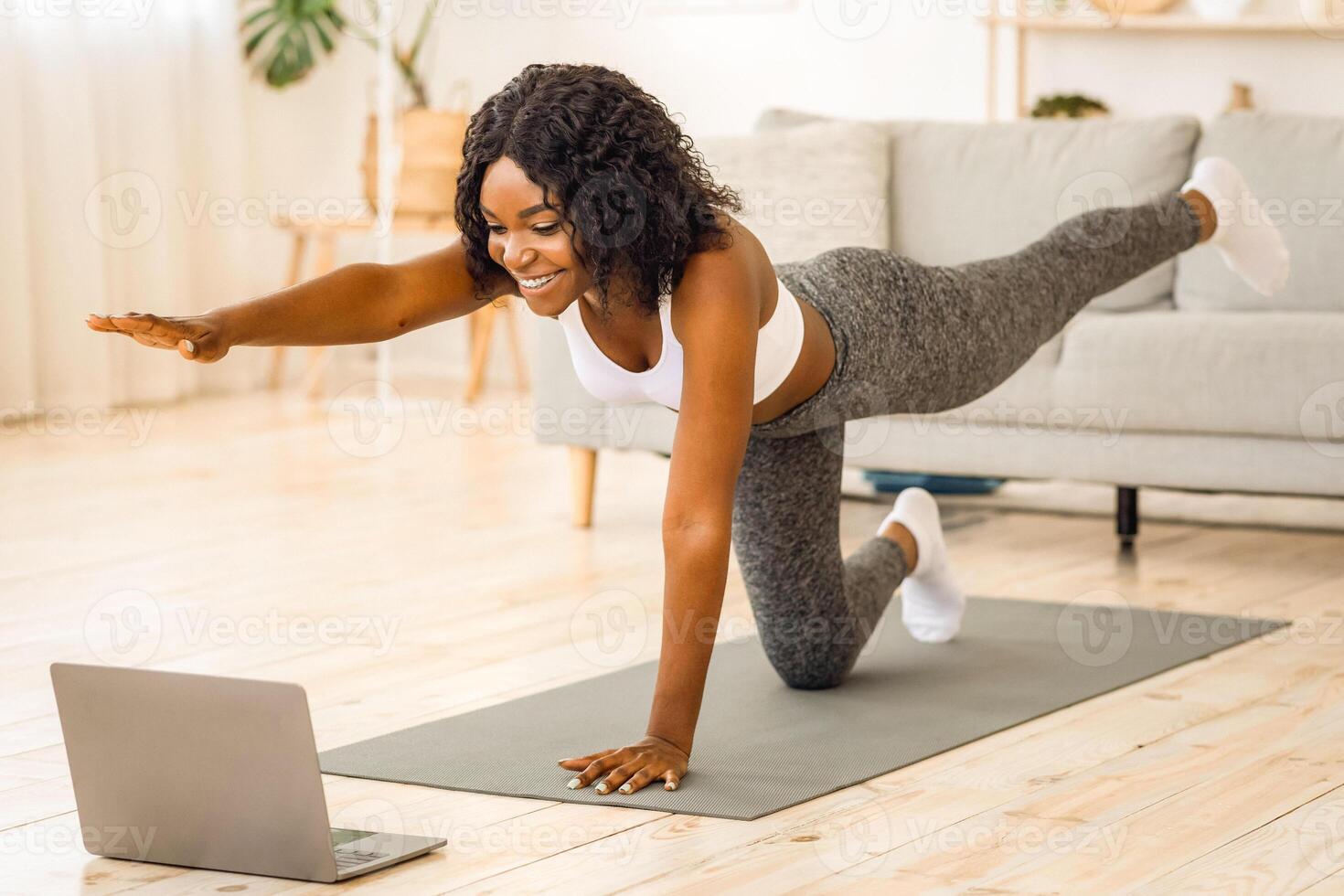 Attractive black woman making morning exercise at home, looking at laptop screen photo