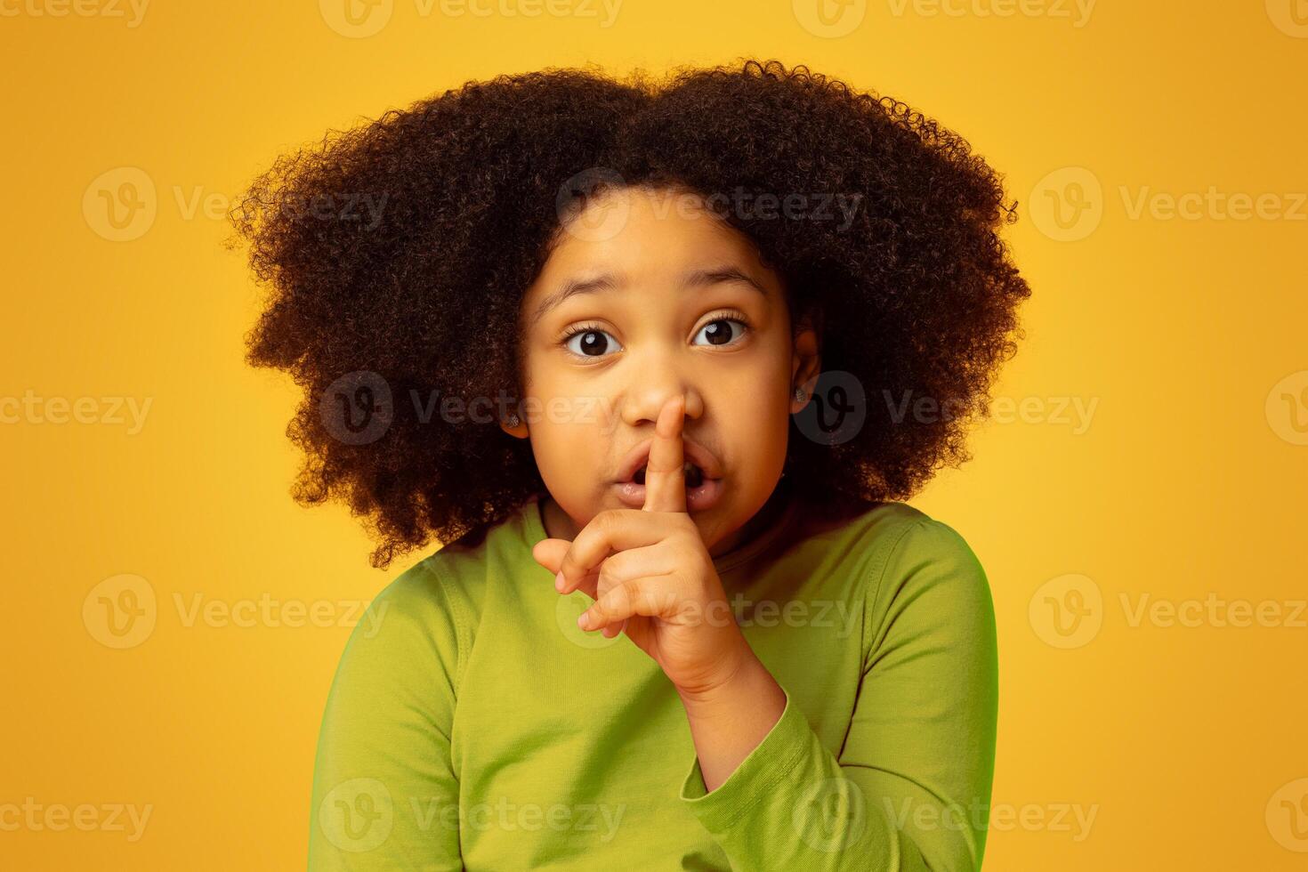 Shh. Serious little african girl showing silence sign, asking be quiet, isolated on yellow background with free space photo
