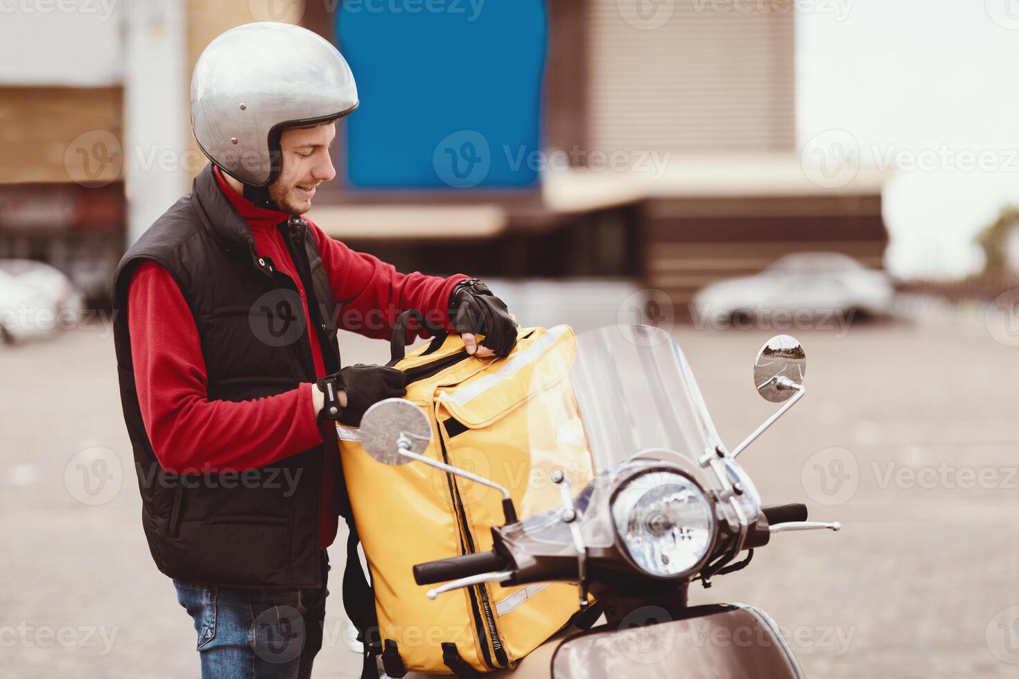 Courier On Scooter Opening Yellow Food Delivery Bag Standing Outside In City. Restaurant Delivering Service photo