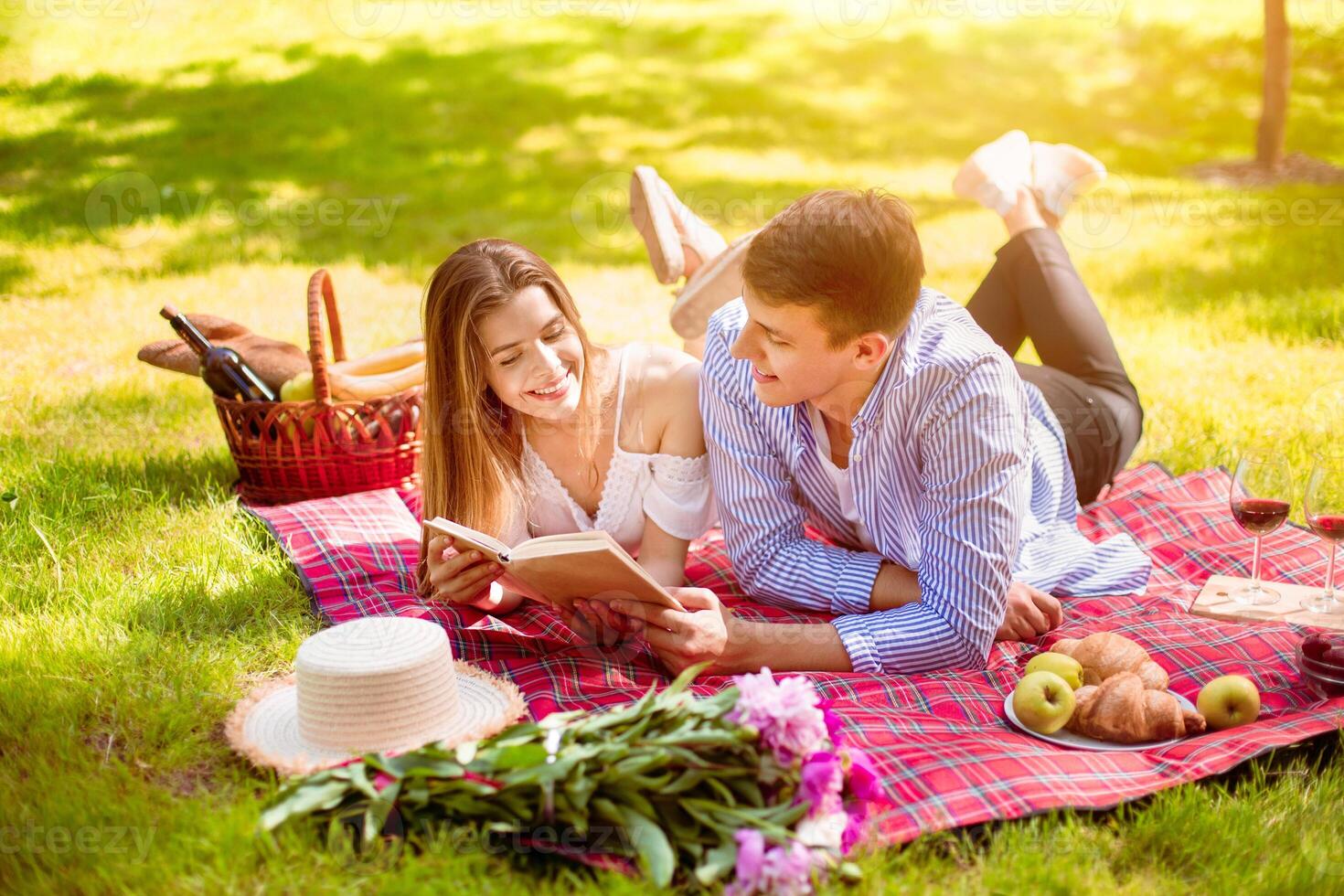 Beautiful married couple reading book while lying on picnic blanket at park photo