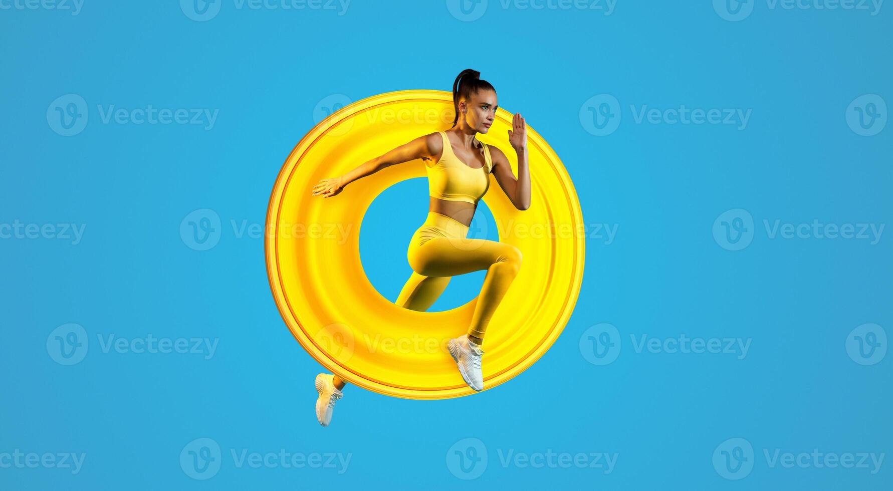 Motivated Young Lady Jumping Posing In Mid-Air Over Blue Studio Background, Looking Aside. Fitness Woman Exercising Wearing Yellow Sportswear Running In Air. Panorama, Full Length Shot photo