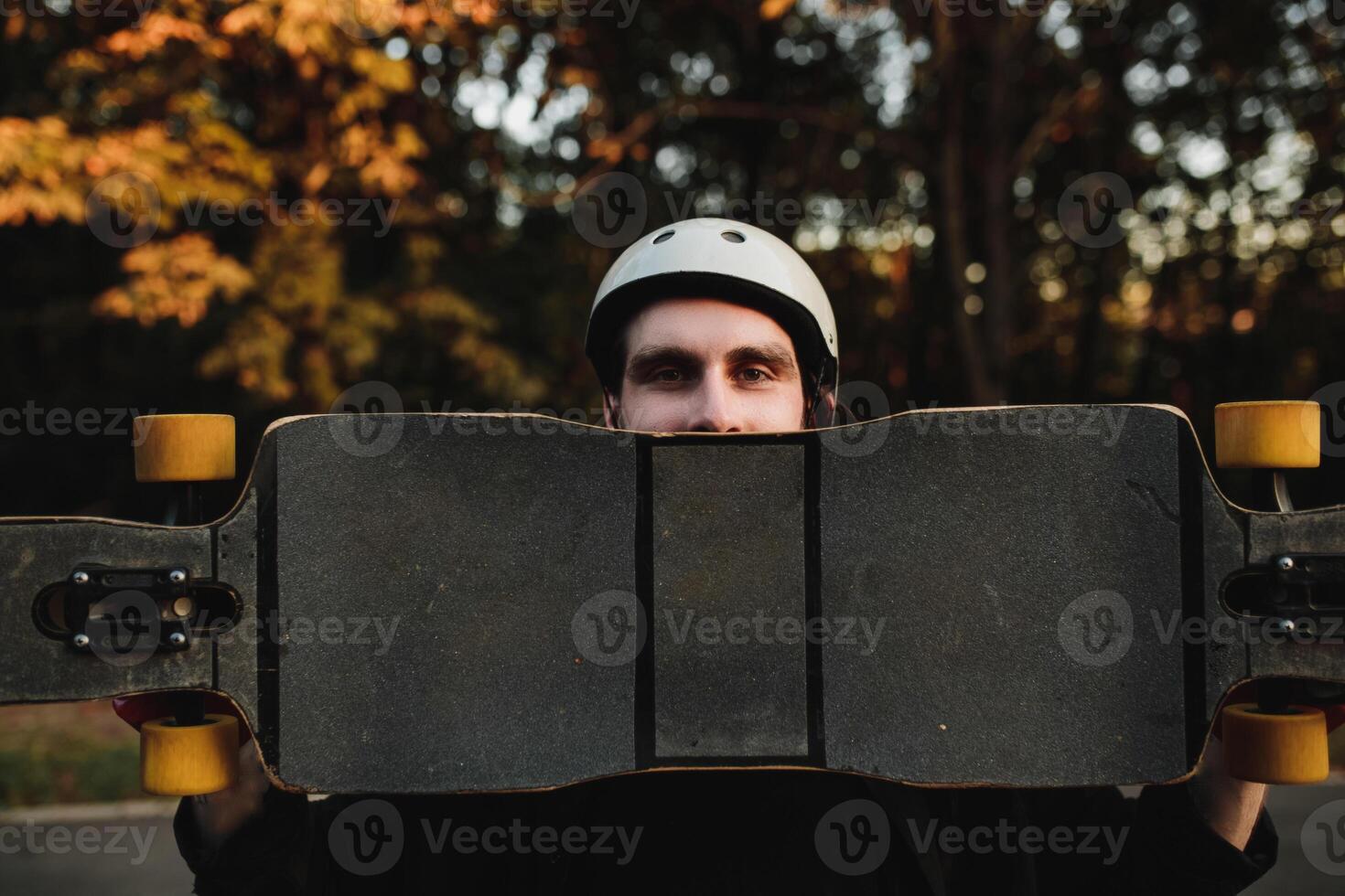 Charismatic guy in a white helmet holds a longboard. photo