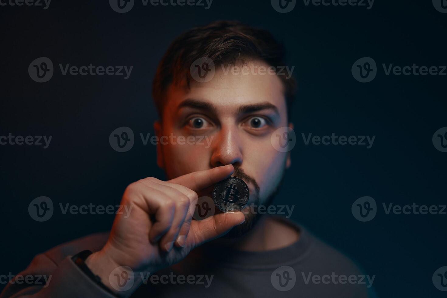 The silence of cryptocurrency. A man holds a coin near his lips. photo
