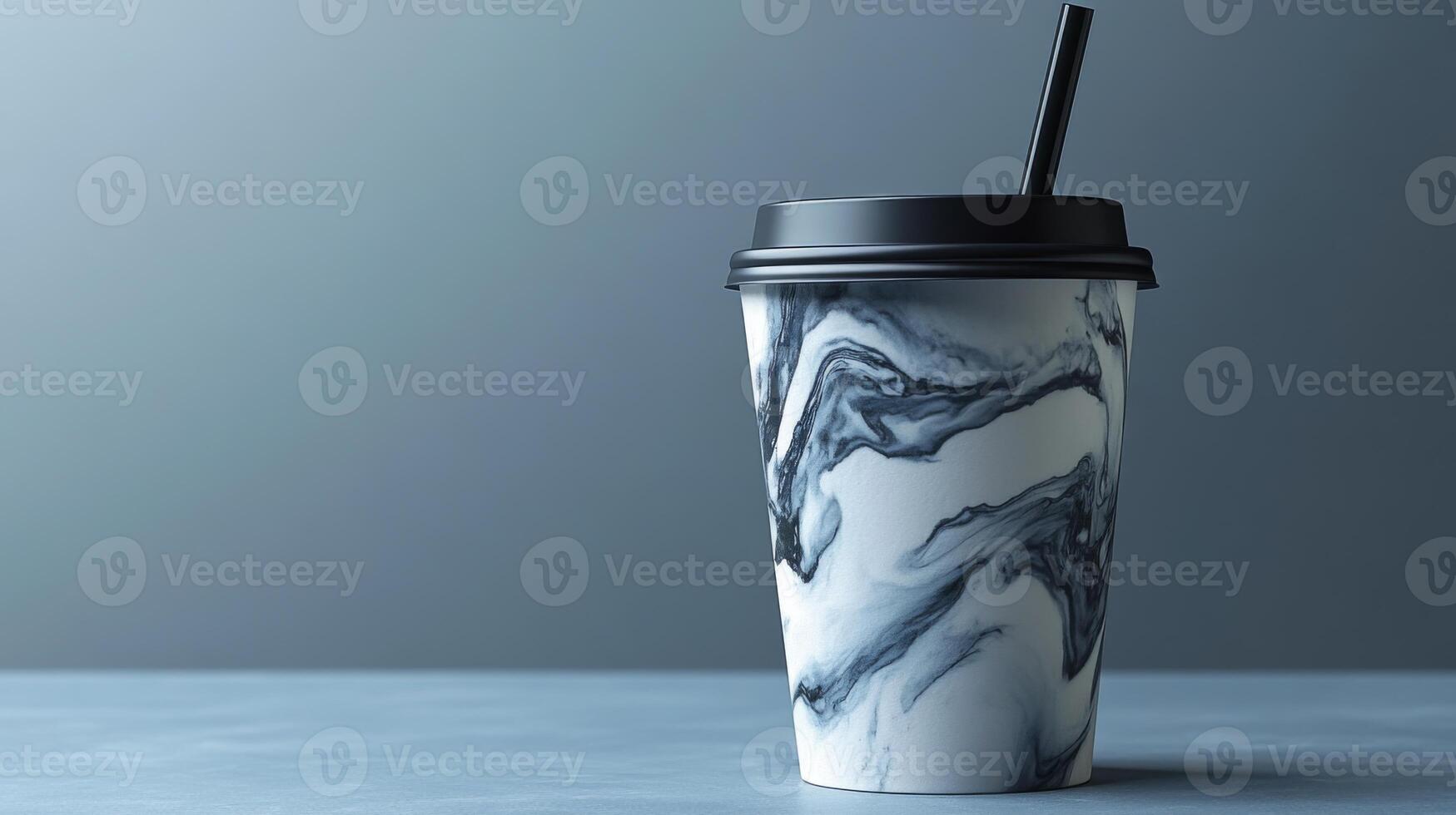 A marbled cup with a black lid and straw rests on a smooth gray surface. The design features swirling black and white patterns, creating a stylish appearance. photo