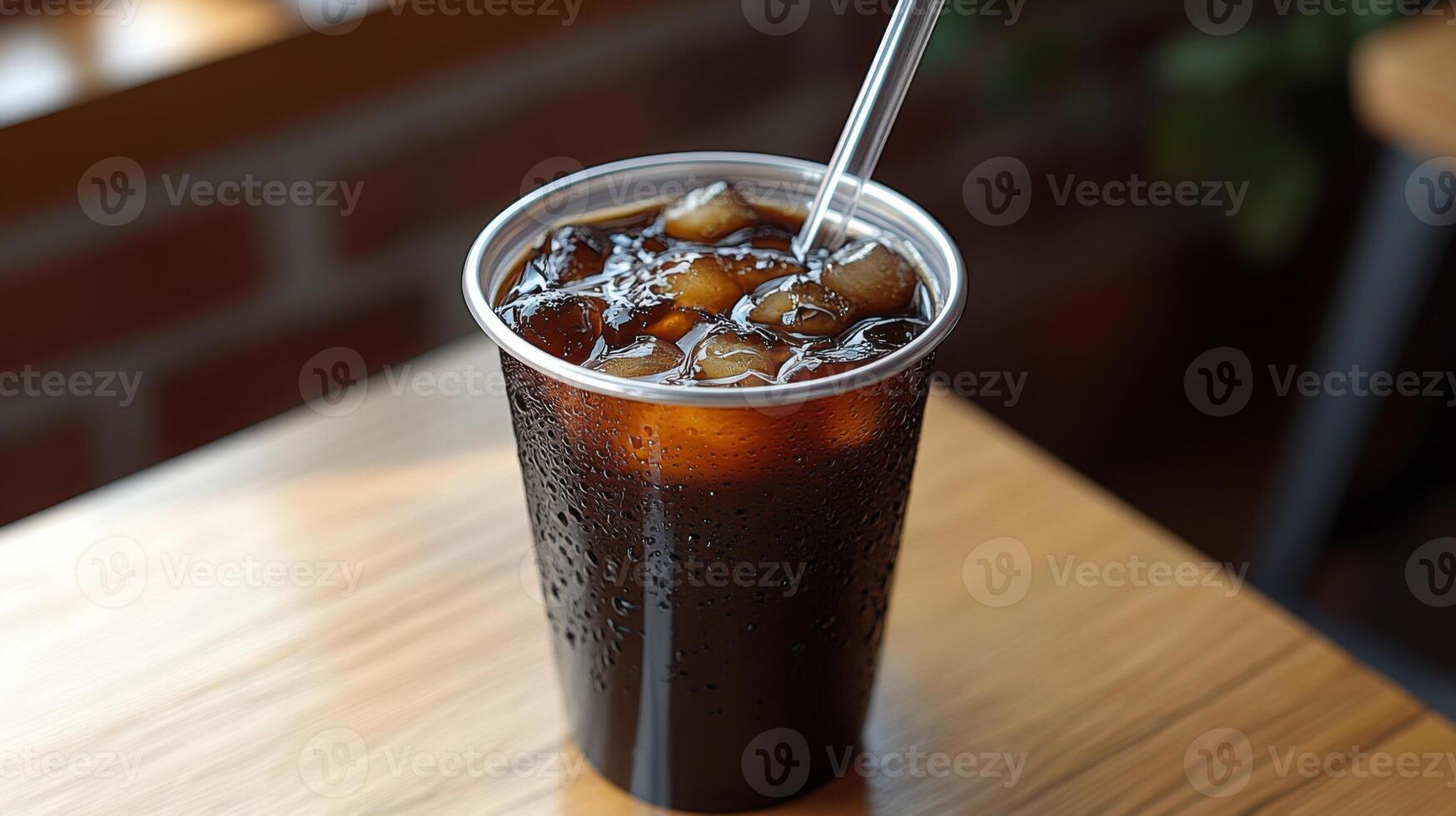 A cold drink filled with ice sits on a wooden table at a cozy cafe. The metal cup shows condensation, indicating the refreshing nature of the beverage enjoyed during midday. photo