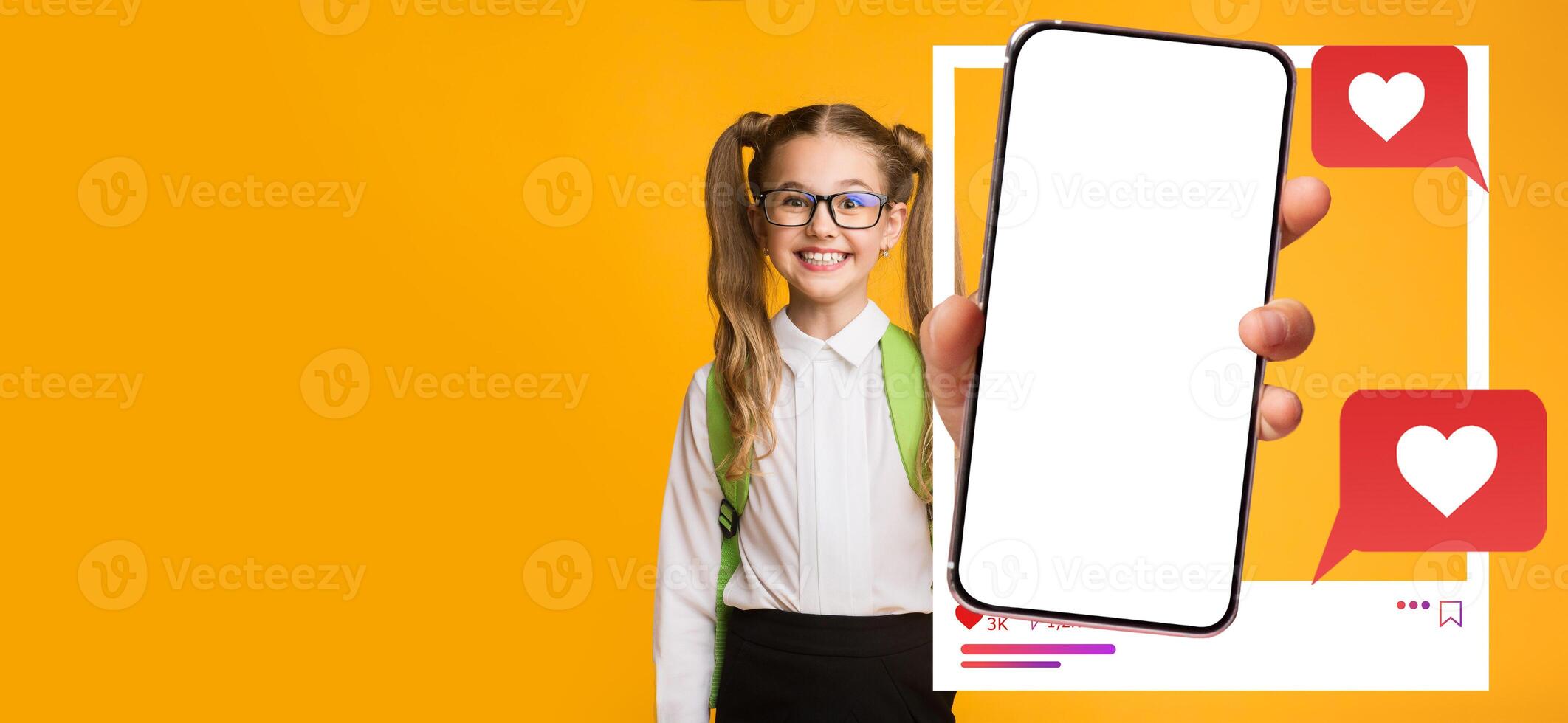 A smiling girl young influencer poses against a vibrant yellow background while holding a smartphone with a blank screen. Heart icons signify engagement with social media apps. photo