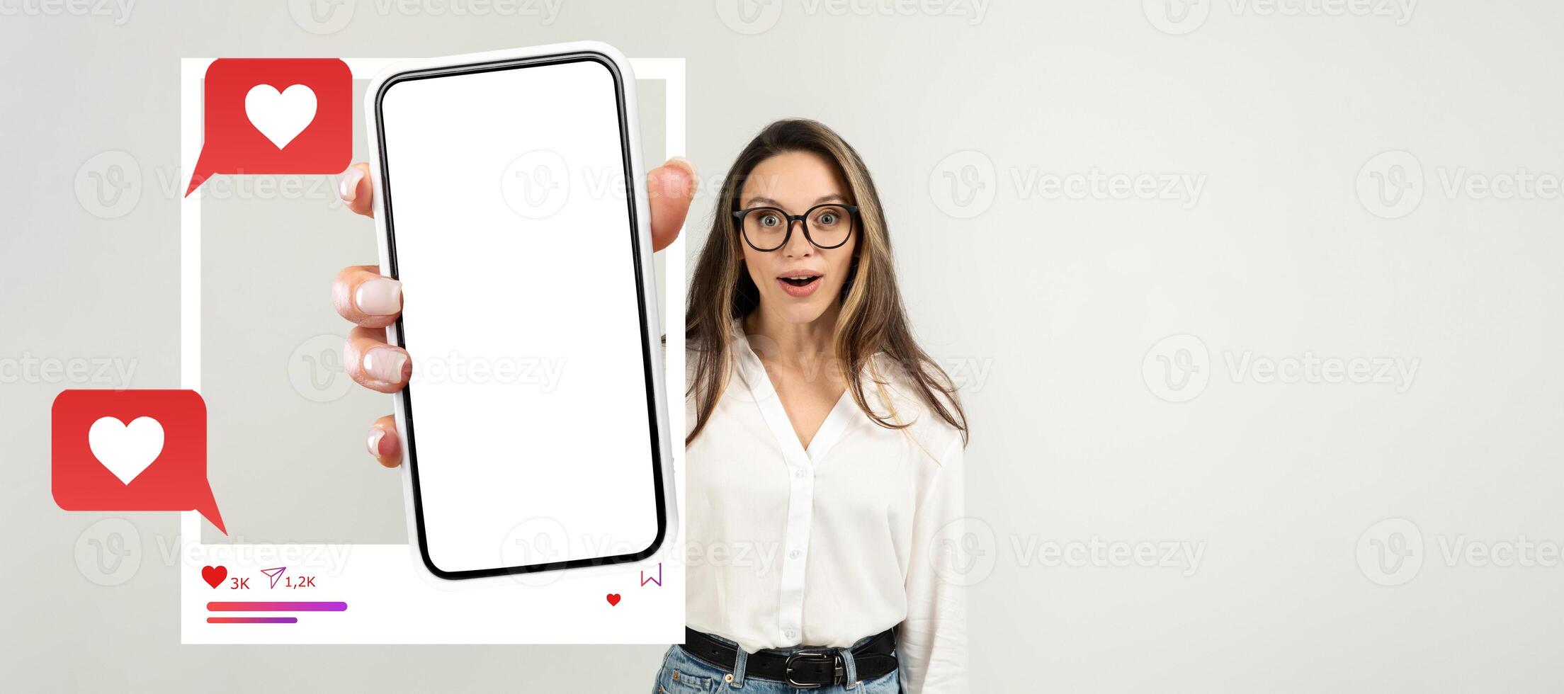 A young influencer with glasses is excitedly holding a smartphone with a blank screen. The background is isolated, highlighting her engaging expression and the potential for social media interaction. photo