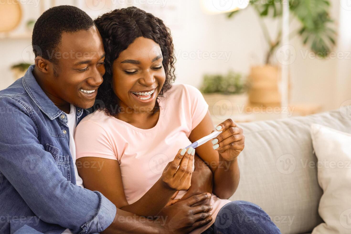 Family and relationships concept. Happy pregnant black couple with pregnancy test at home, hugging and smiling, free space. Emotional african american man and woman ready to become parents photo