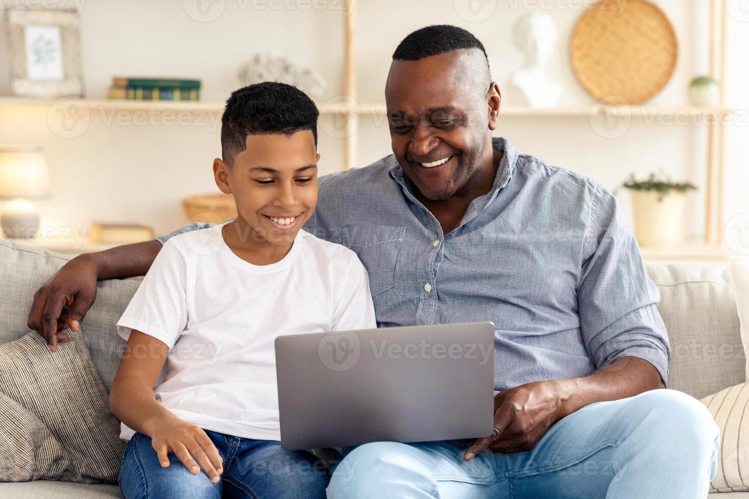 A father and son engage in a delightful moment, sharing smiles and laughter while exploring content on a laptop in a cozy living room on a weekend afternoon. photo