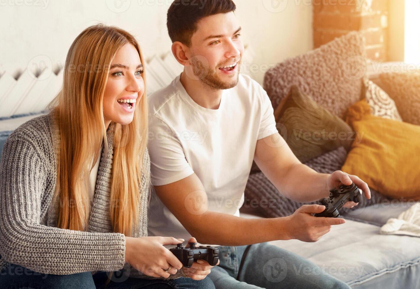 A couple joyfully engages in a gaming session, sharing laughter and excitement. They sit comfortably on a sofa surrounded by soft cushions, soaking in the warm light from the window. photo