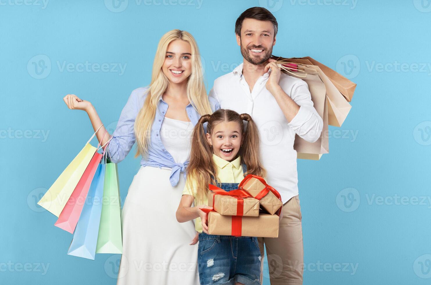 Holiday Gifts Shopping. Parents And Daughter Holding Wrapped Boxes And Shopper Bags On Blue Studio Background. photo