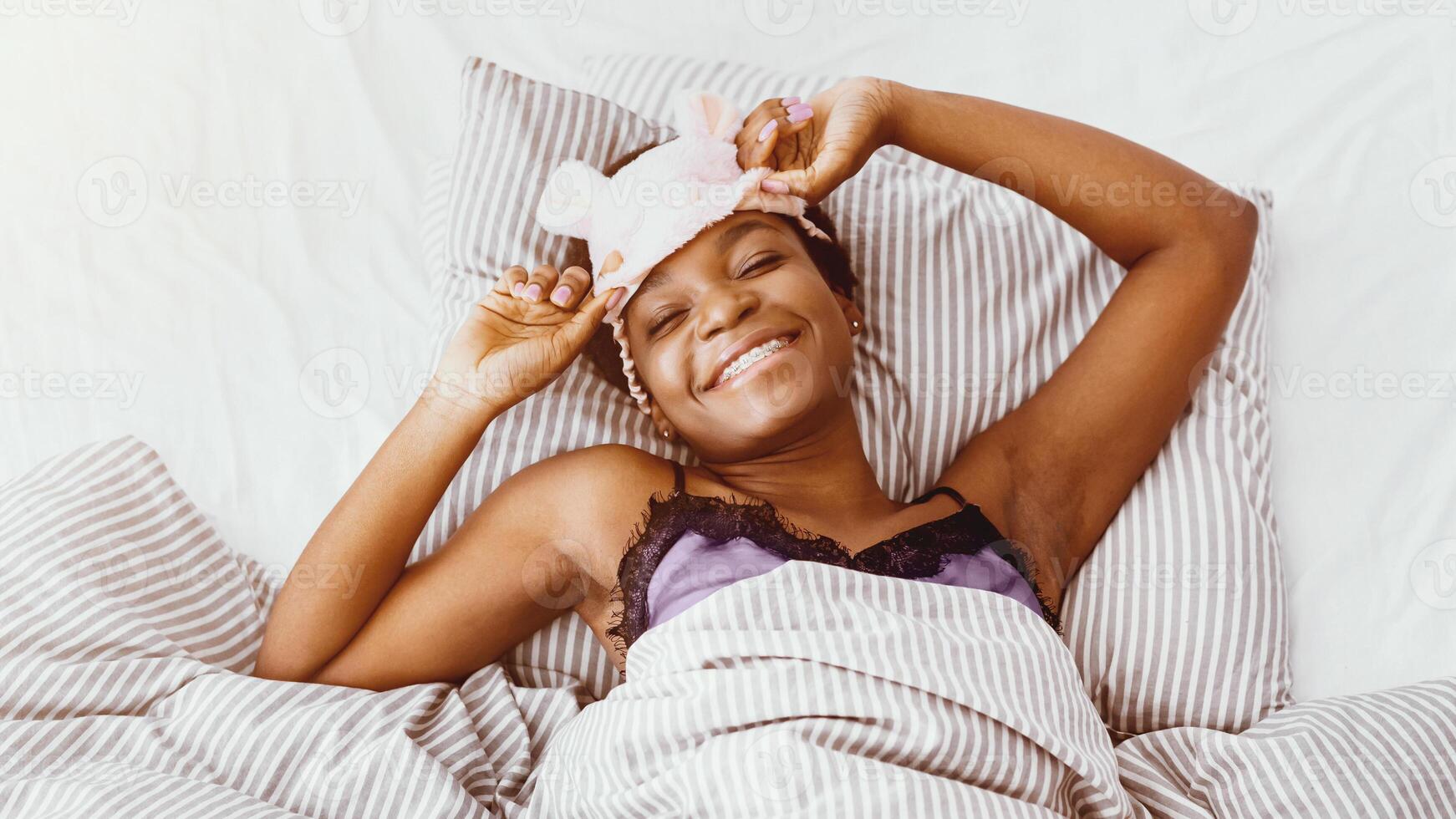 Wake up with smile. Happy african american girl with braces in bed takes off her sleeping mask, close up, panorama, free space photo