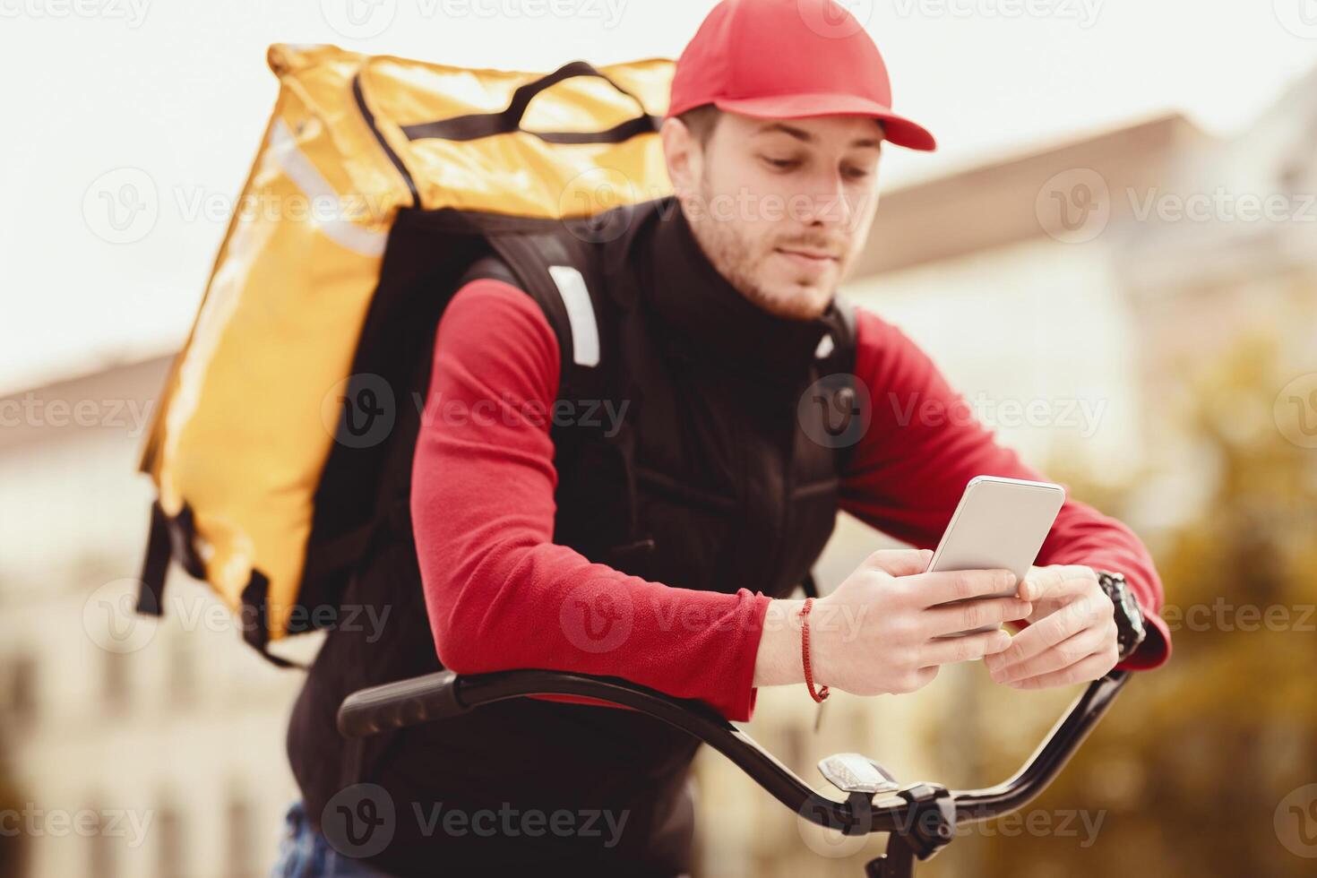 Courier Using Delivery Application On Mobile Phone Delivering Food In Yellow Bag Sitting On Bicycle In City. Shallow Depth photo