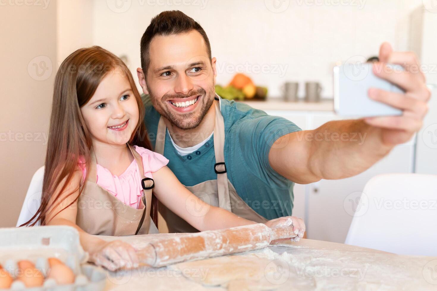 Happy Dad And Daughter Making Selfie On Phone Baking Cookies Together Posing Rolling Out Pastry Dough In Modern Kitchen At Home. Cute Fatherhood Moments Concept. Selective Focus photo