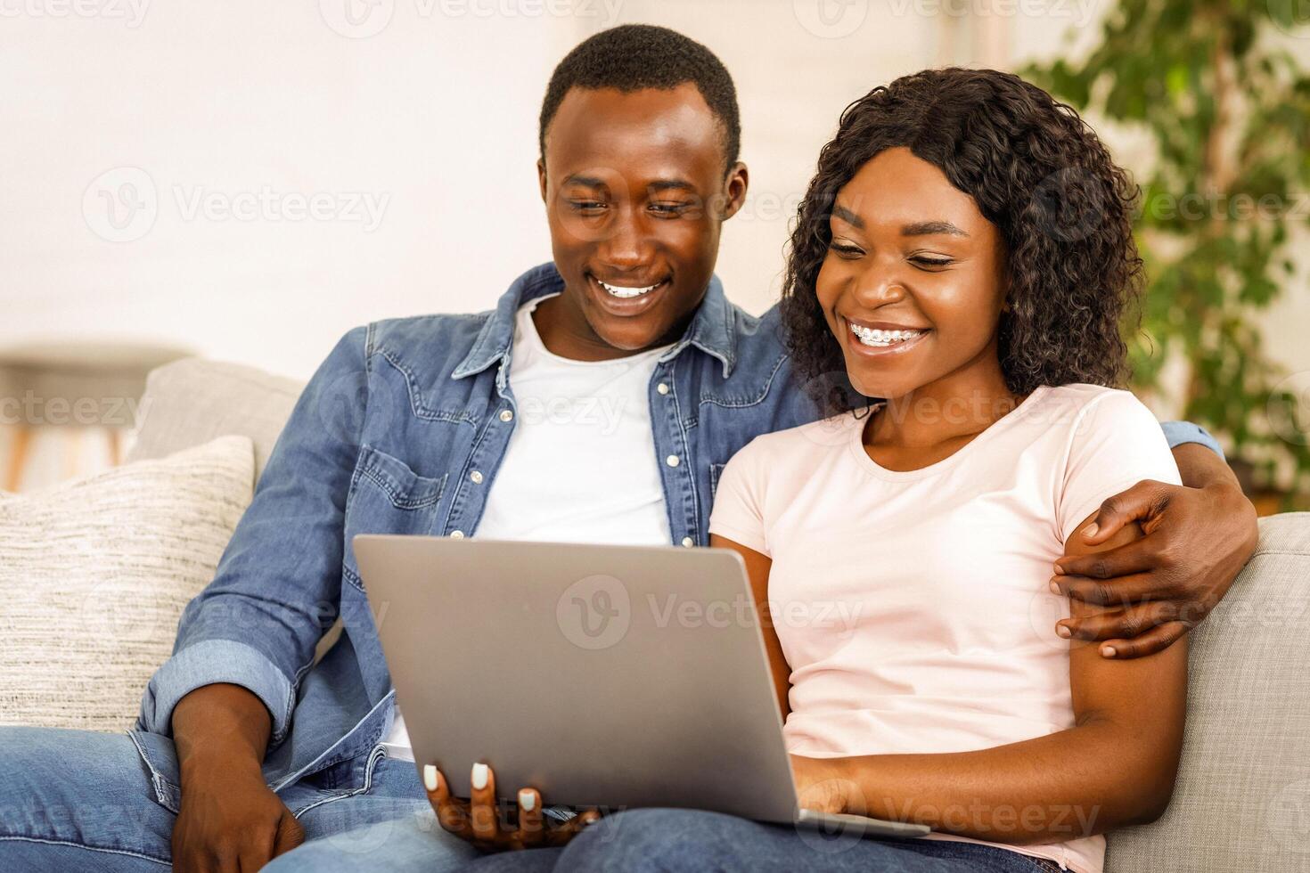 Lovely black couple using laptop while resting on couch at living room at home, watching photos together