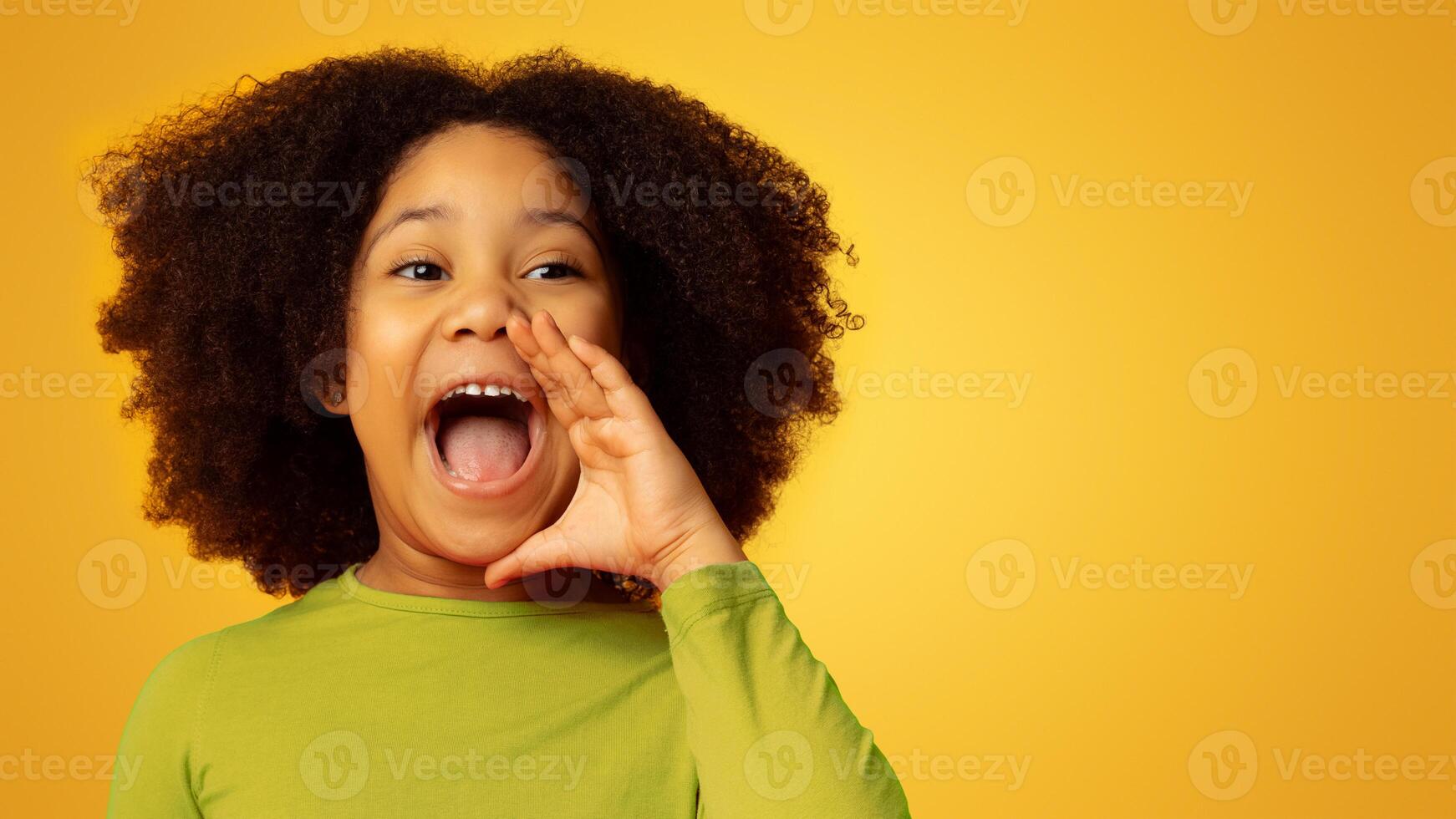 Funny little african american girl emotionally screaming, making announcement, loudly shouting with her hand near mouth, yellow background photo