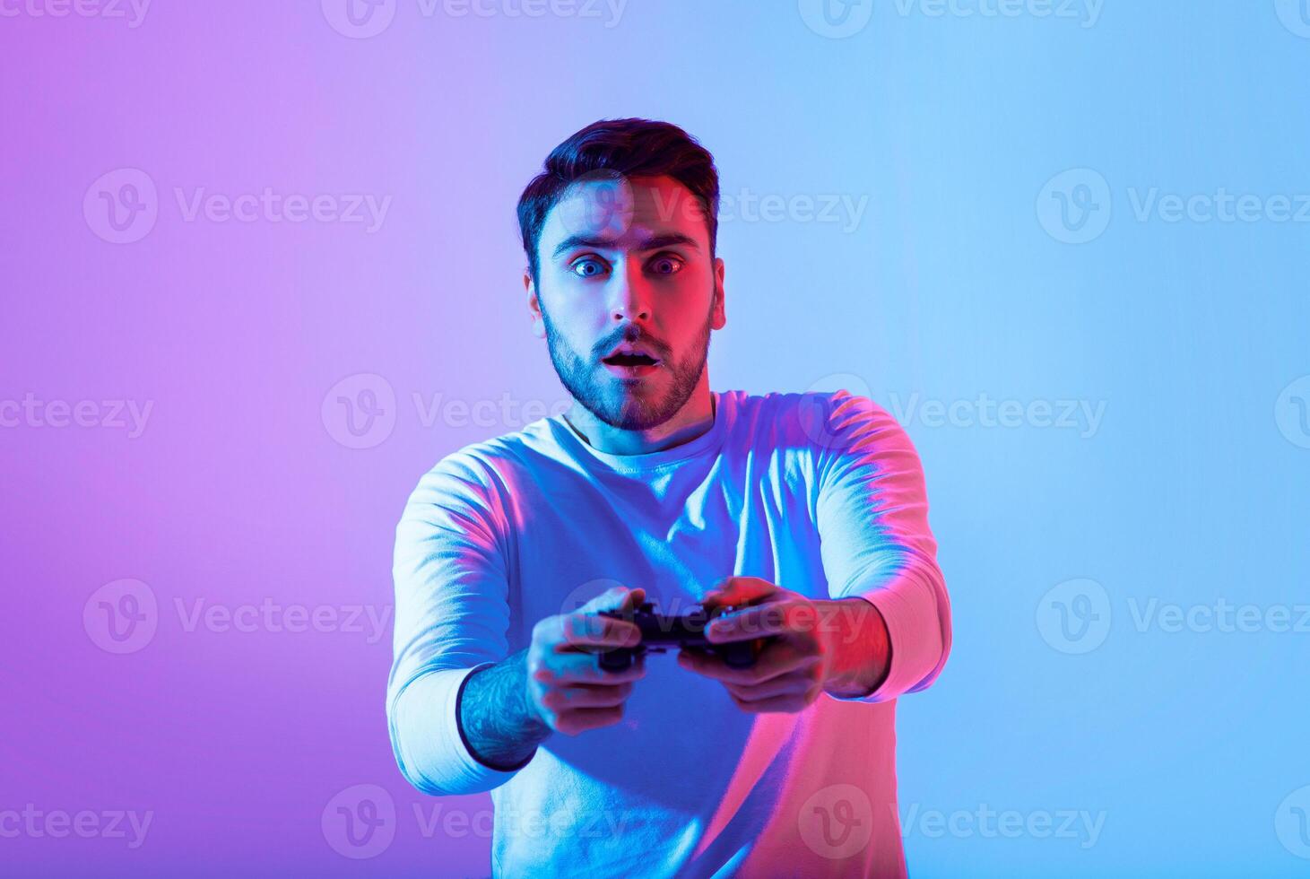 A young man expresses surprise while playing a game, holding a controller. Colorful blue and purple lighting enhances the excitement of the gaming experience. photo