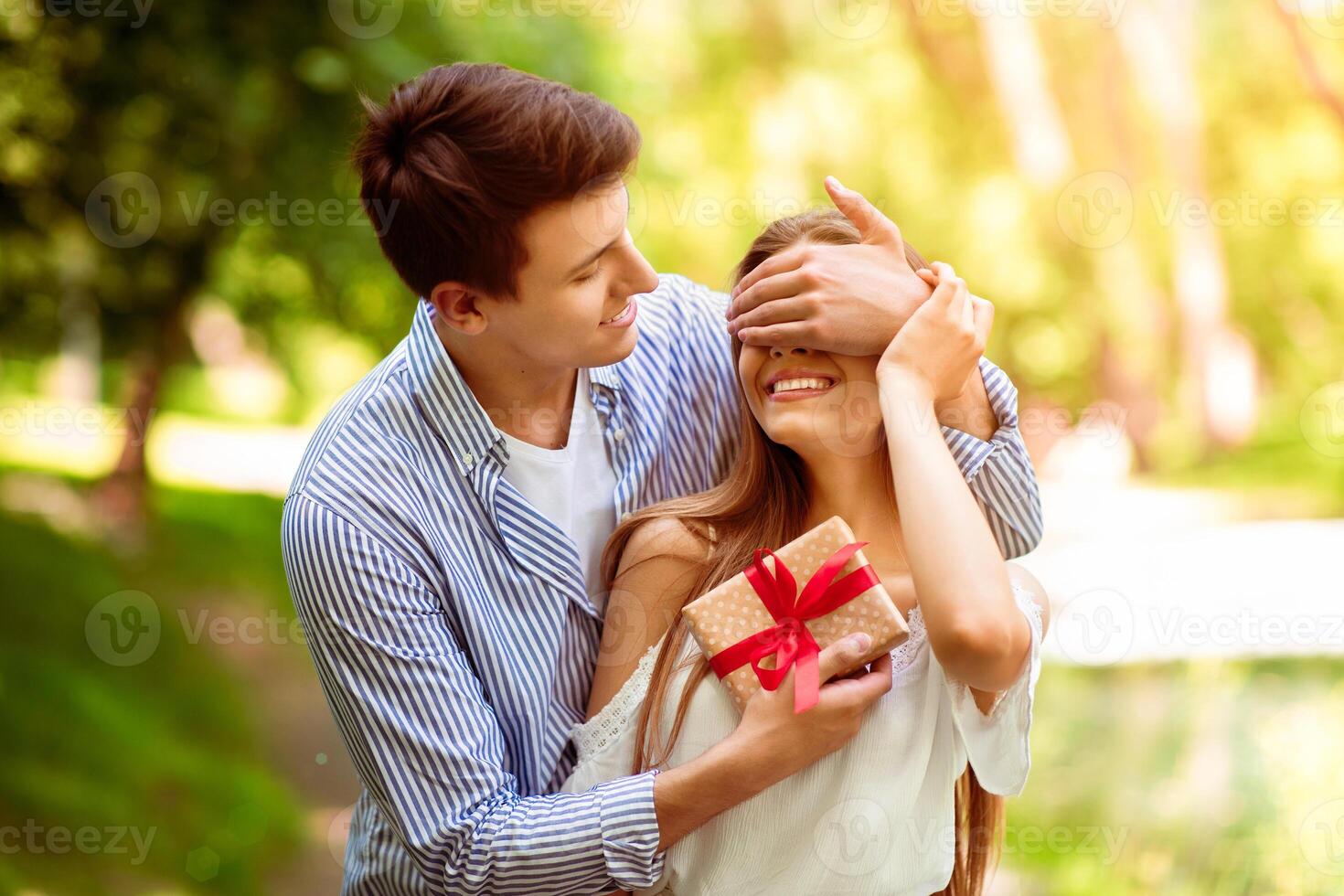 Caring boyfriend surprising his girl with unexpected gift at beautiful summer park photo