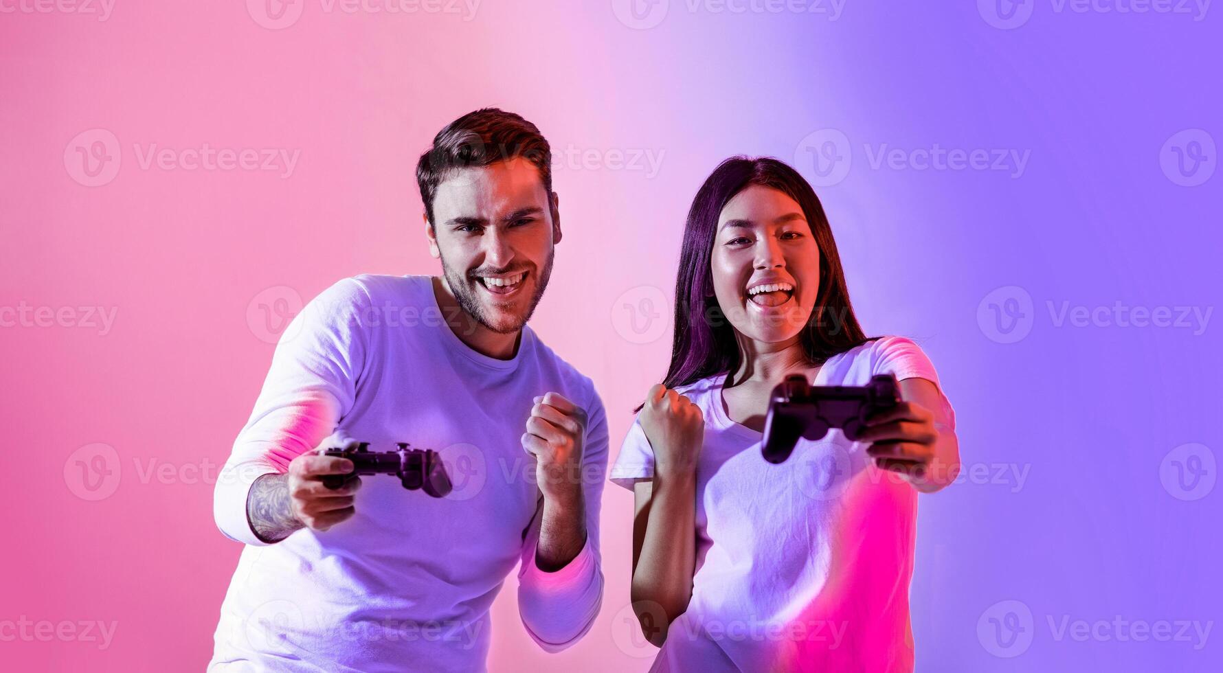 Two friends are joyfully playing games with controllers in hand. They share smiles and excitement, surrounded by a vibrant backdrop of purple and pink hues. photo