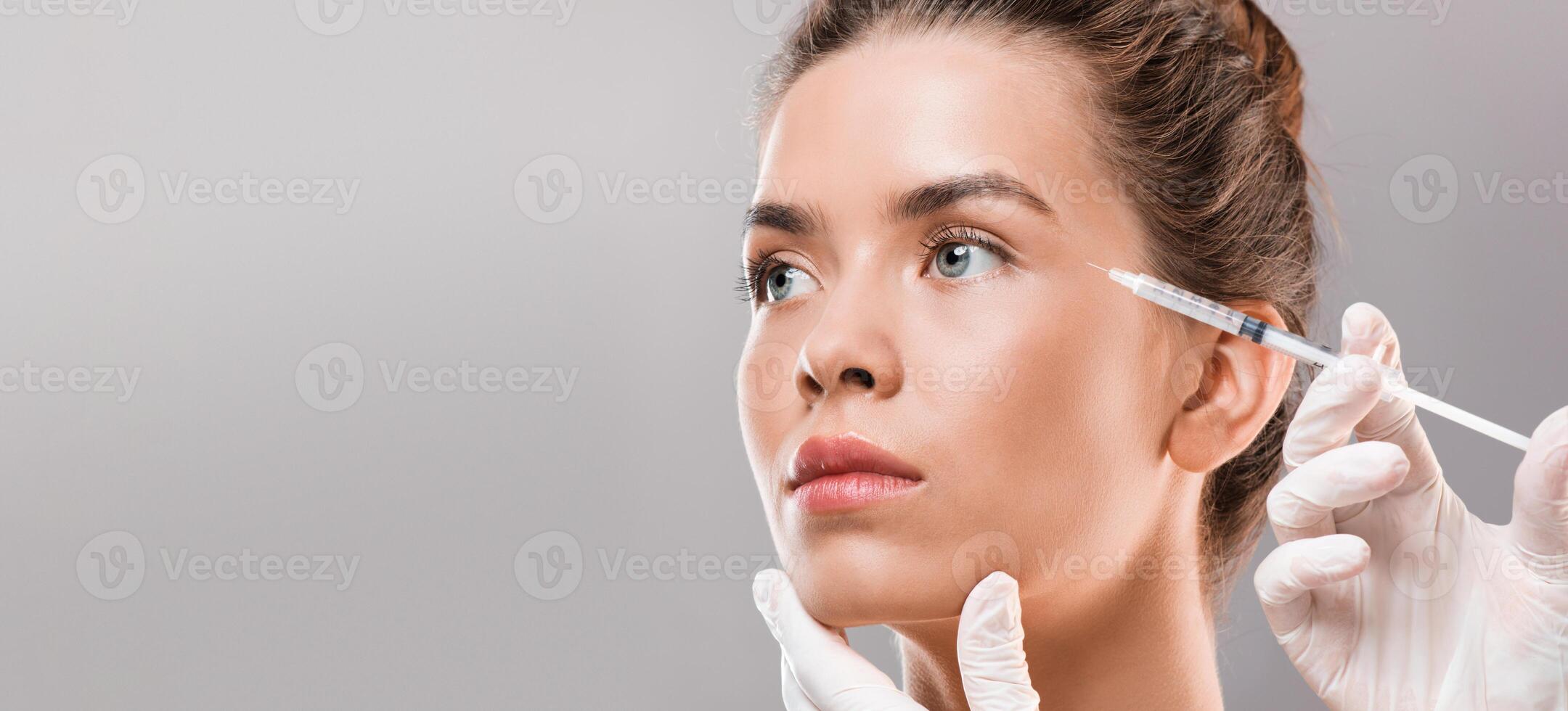 Young beautiful woman getting beauty injection for eyes area over grey studio background, closeup, copy space photo