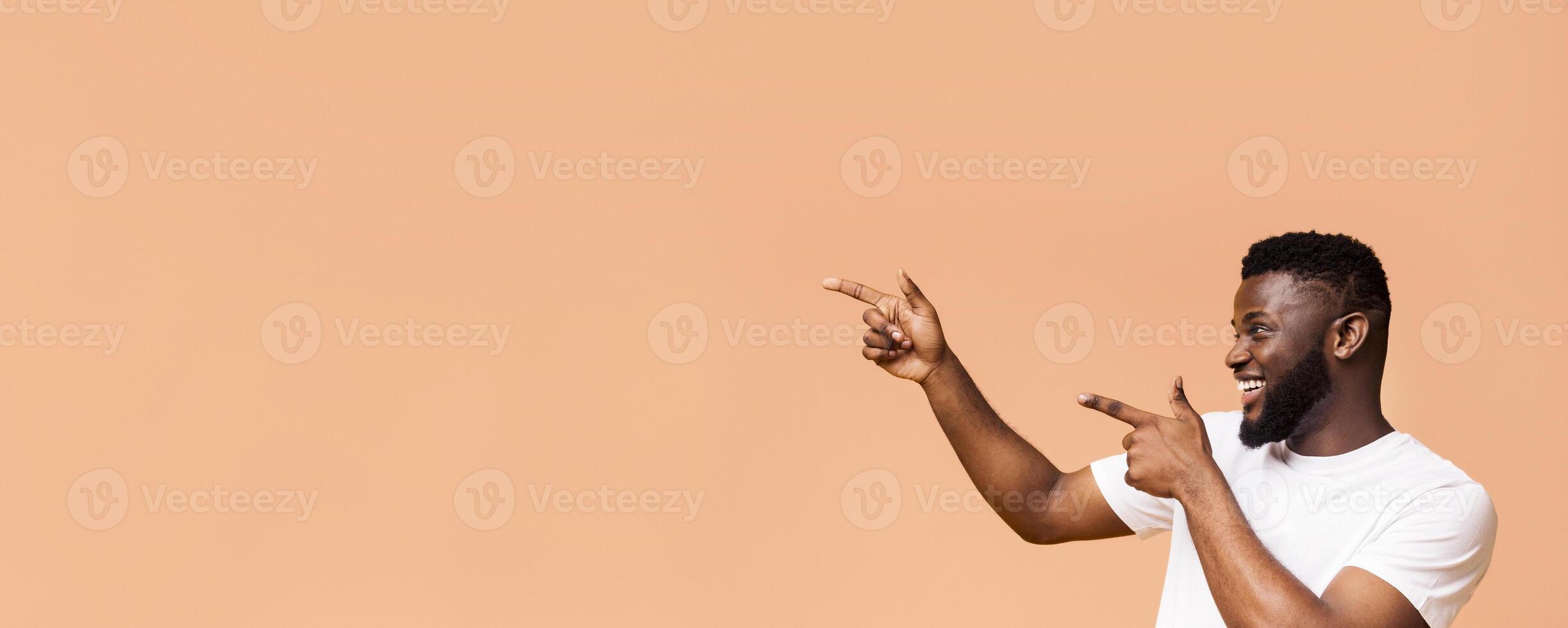 Look over here. Positive african american guy pointing both hands aside at free space, orange panorama background photo