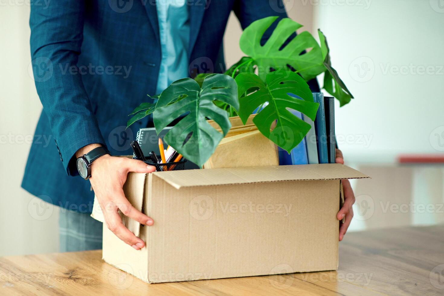 A young Middle Eastern businessman is transporting a box filled with office supplies and potted plants in a modern office setting, reflecting an active corporate lifestyle. photo
