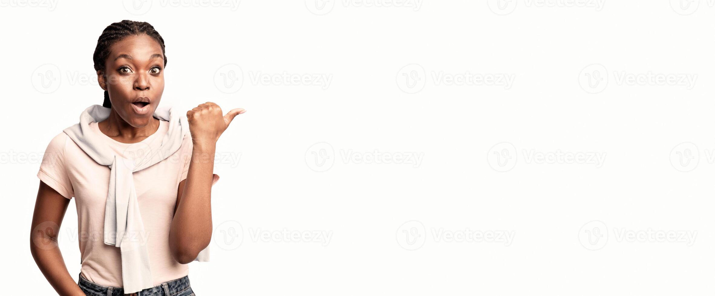 A young woman with braided hair displays a surprised expression, enthusiastically pointing left. photo