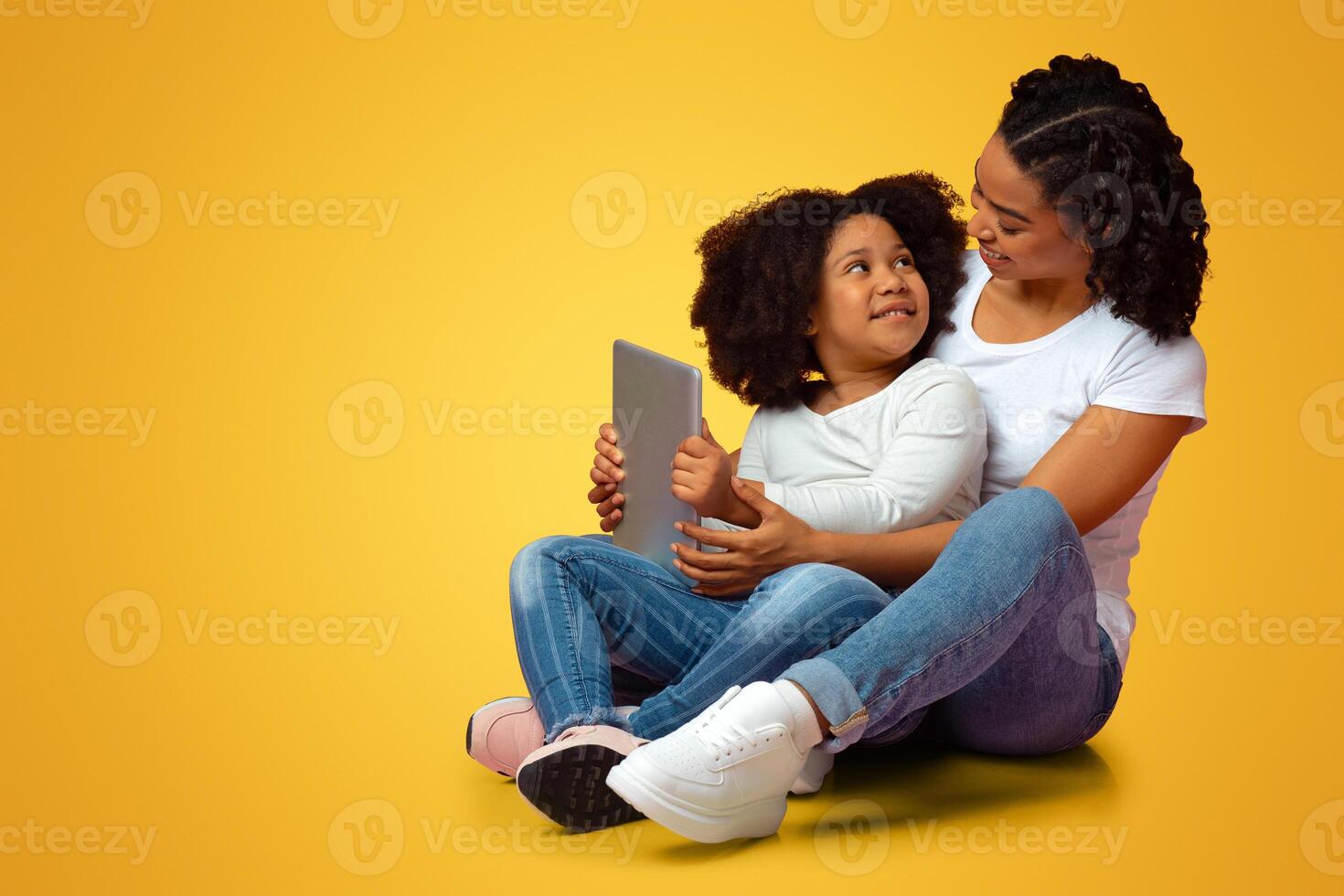 Modern Technologies For Kids. Little Black Girl Holding Digital Tablet While Sitting In Lap Of Loving Mom, Pink Studio Background, Empty Space photo