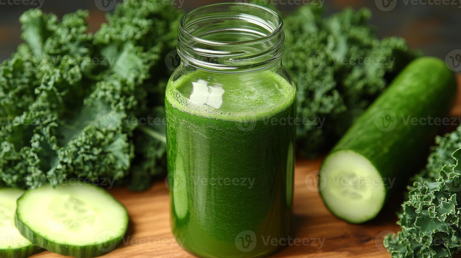 A refreshing green smoothie sits in a glass jar, made with kale and cucumber, resting on a wooden surface with sliced cucumbers and whole kale nearby. photo