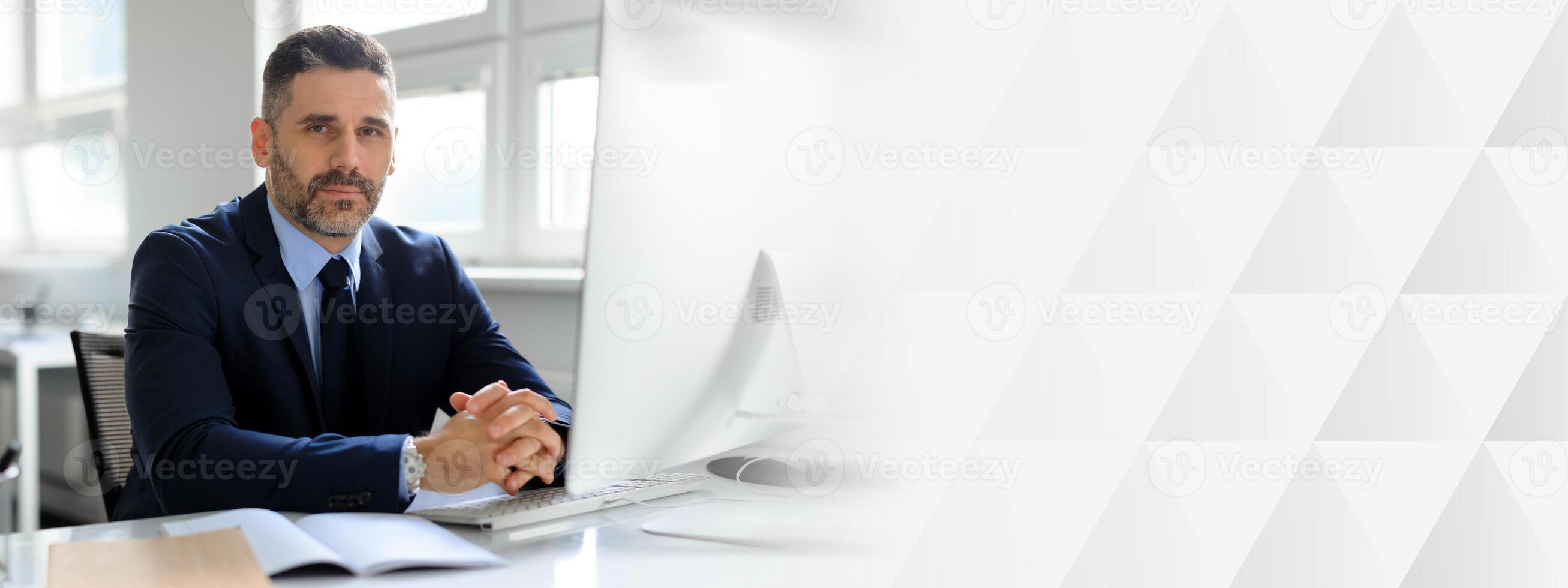 A middle aged businessman sits attentively at his desk in a well-lit office. He is dressed in a suit and appears to be working diligently, embodying a successful lifestyle, copy space photo