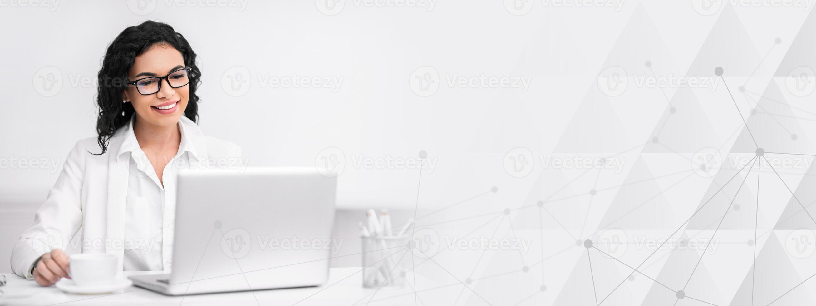 Assistant. Portrait of happy mexican woman in glasses working on laptop, drinking coffee, copy space photo