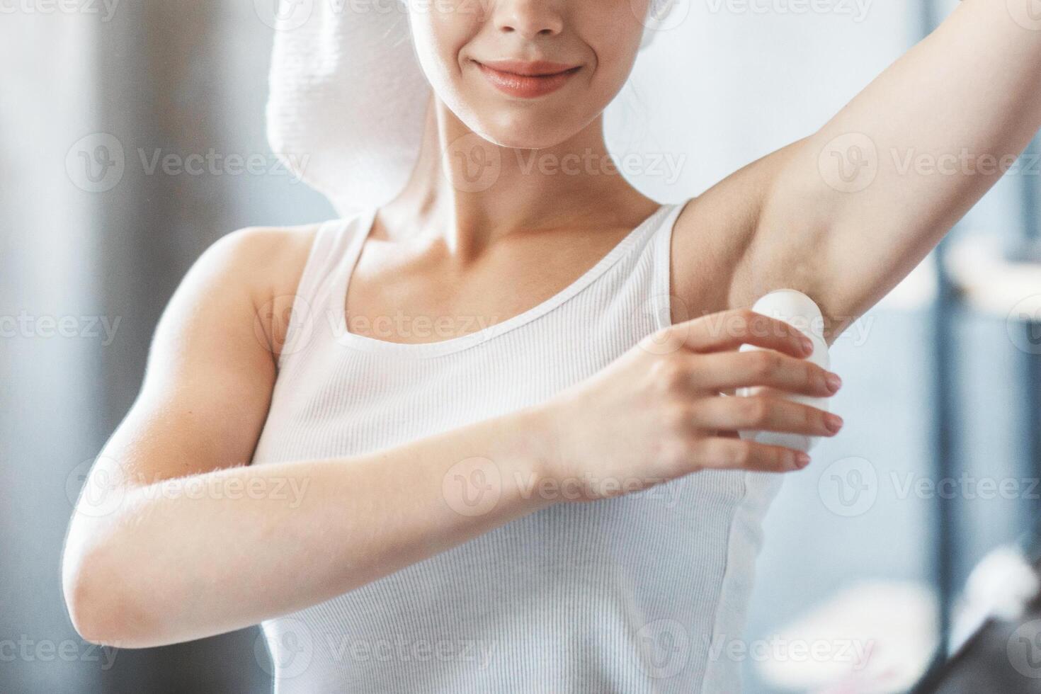 Millennial Caucasian girl using roller deodorant after shower near mirror at bathroom photo