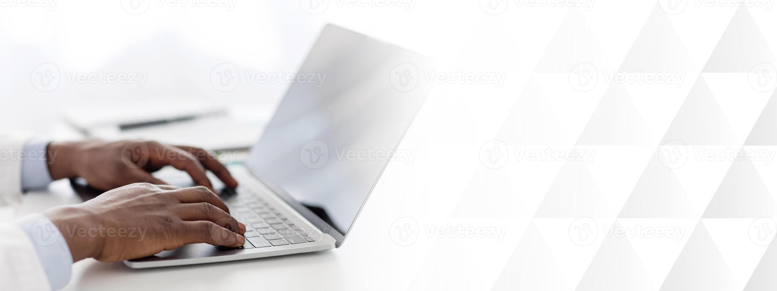 Modern medicine. African american man doctor using laptop computer with blank black screen, sitting at workplace in office, closeup, crop. Mockup for ad photo