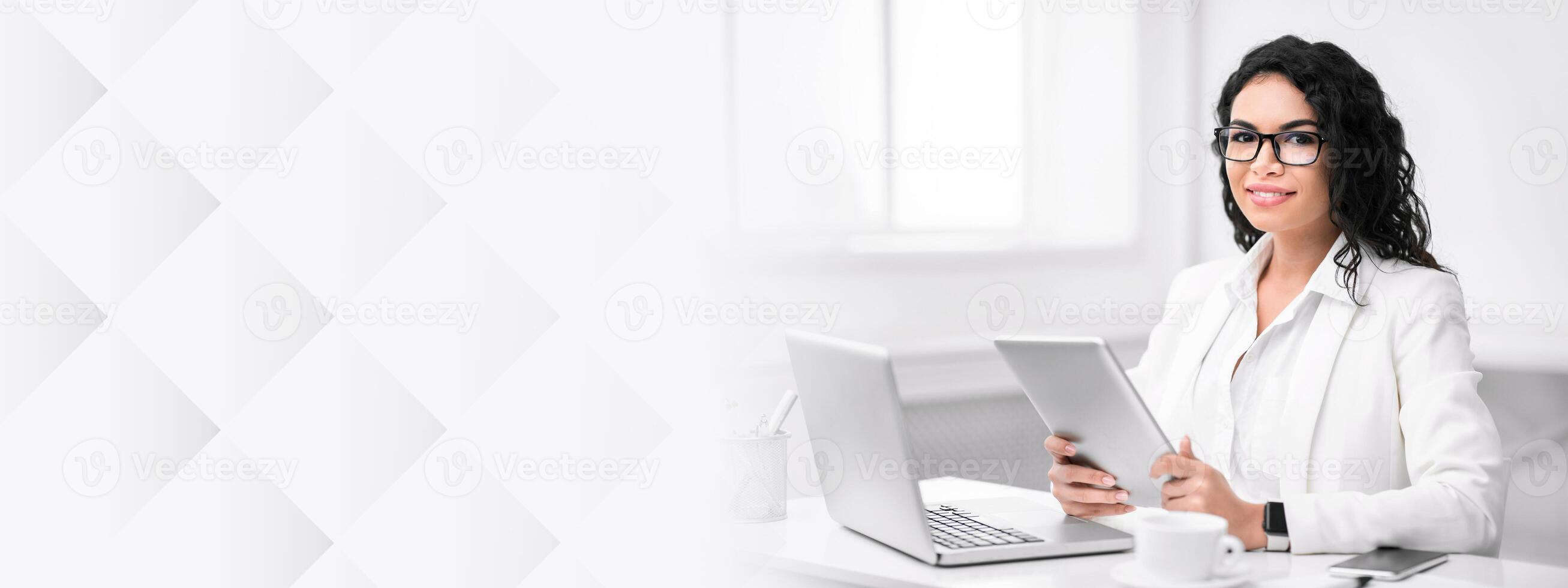 Busy Woman. Confident latin lady using laptop computer, holding digital tablet, looking at camera, copy space photo