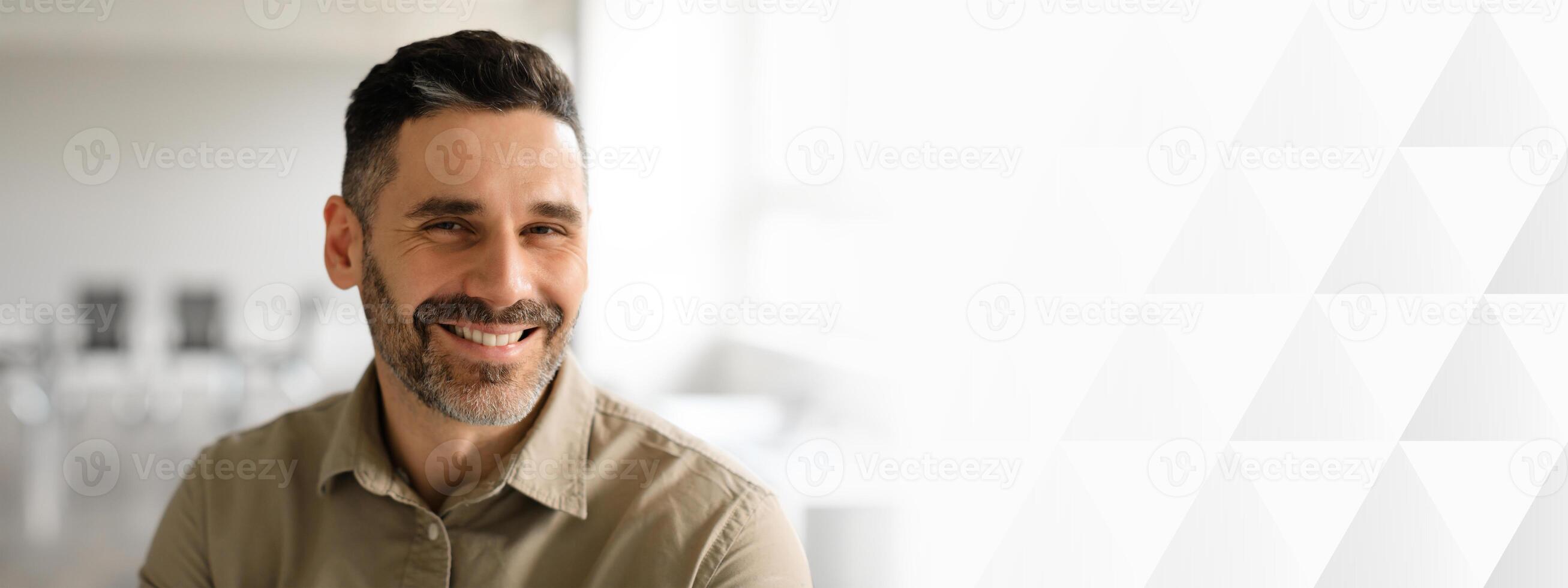 A middle aged businessman with a beard is smiling while seated in a modern office. Natural light floods the space, enhancing the professional atmosphere and his entrepreneurial spirit, copy space photo