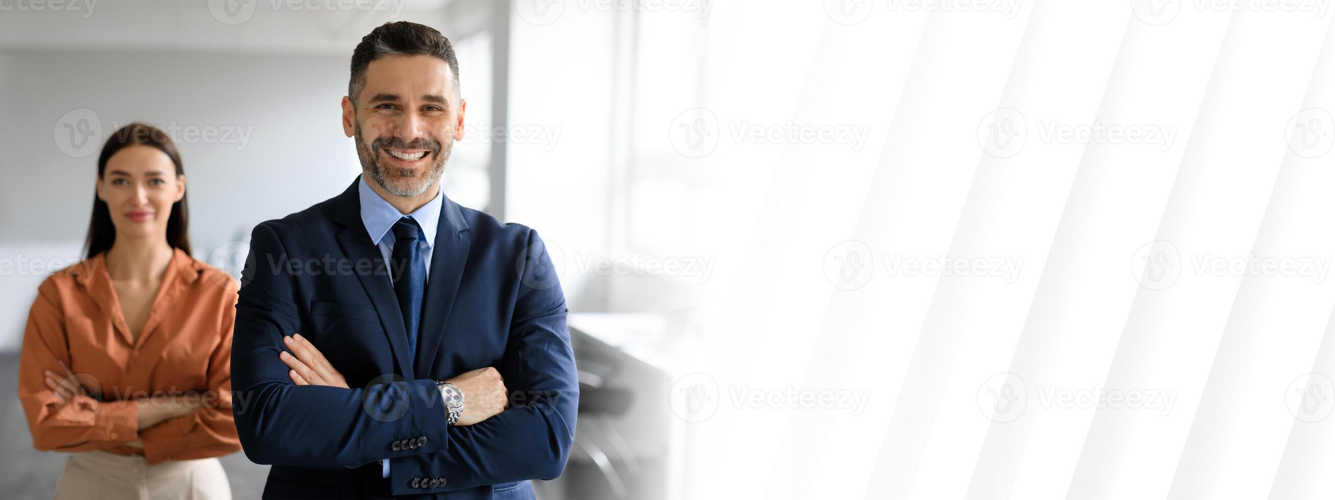 A businessman and businesswoman stand confidently in a well-lit office, symbolizing teamwork and success. Their professional attire reflects a dynamic corporate environment conducive to cooperation. photo