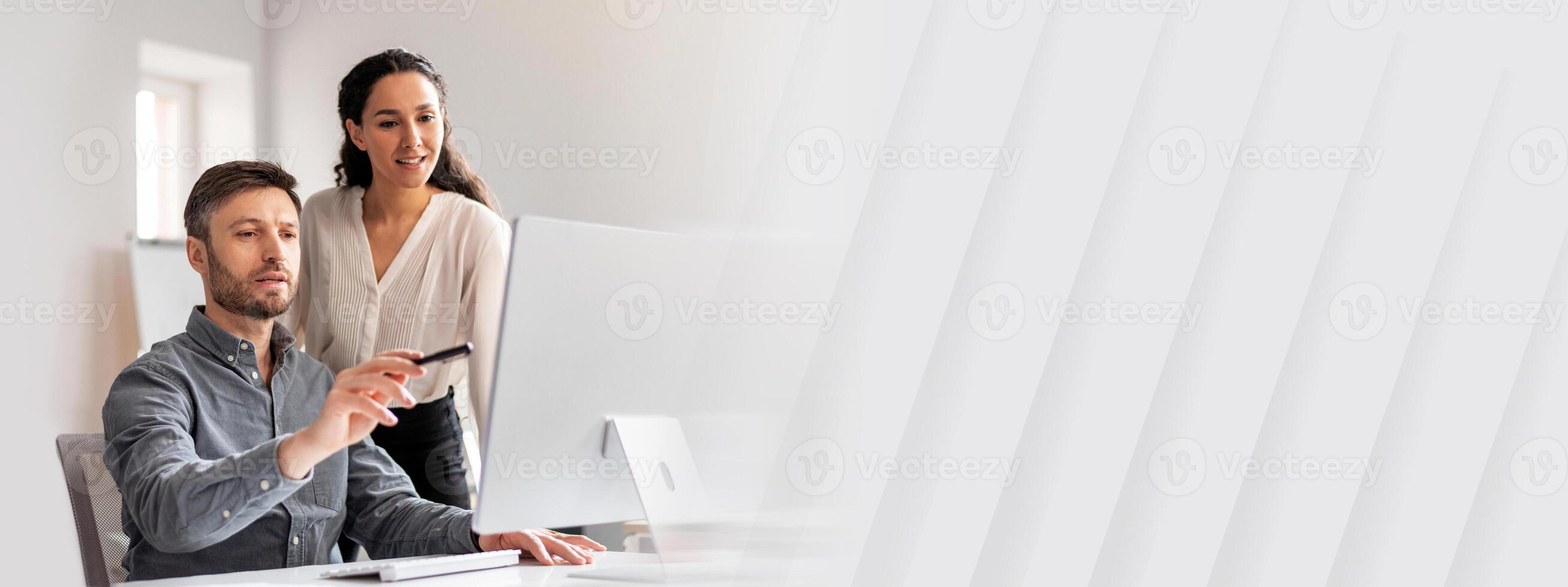 Cheerful young caucasian man manager show to lady with hand at computer in modern office interior, free space. Business teamwork, finance plan, data analysis, developing in company and work together photo