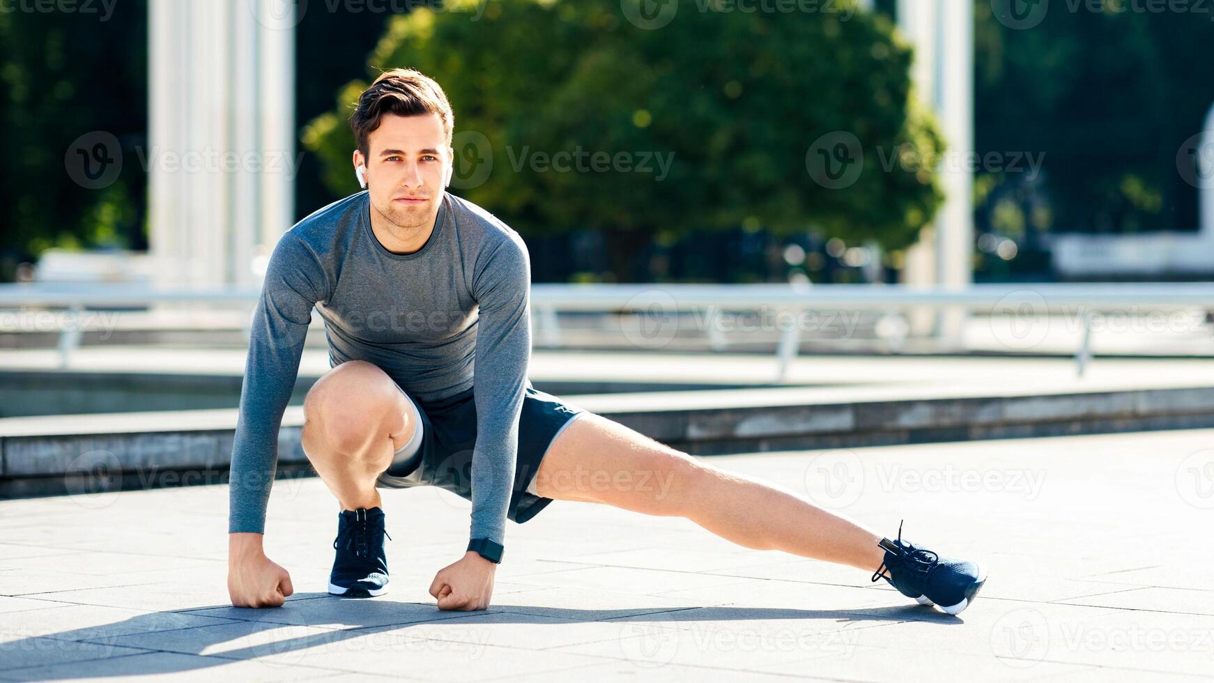 Exercises for warming up muscles before training. Attractive guy in sportswear training in park with green trees, free space photo
