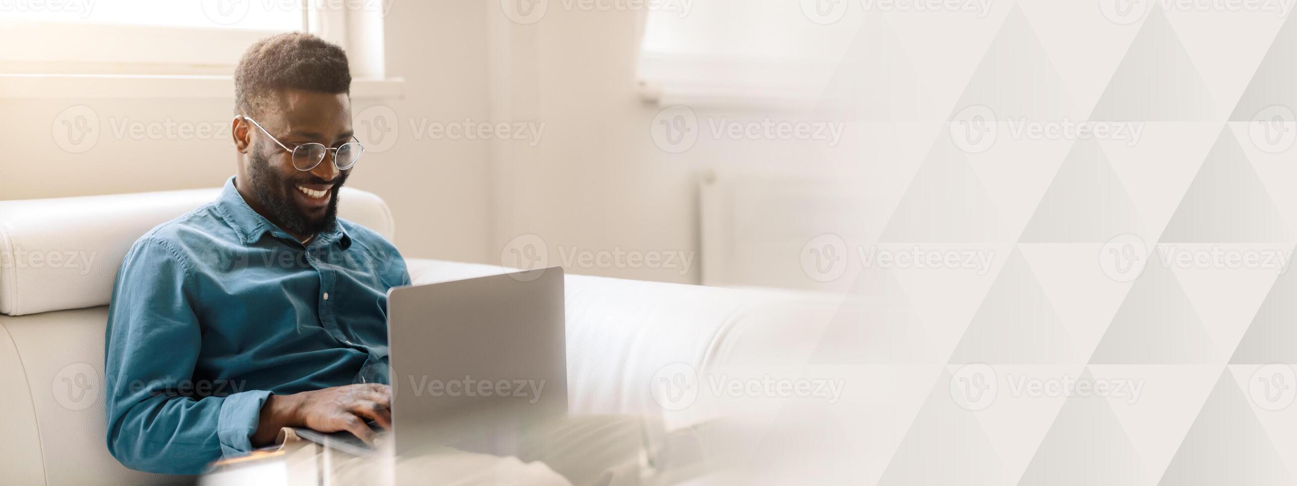 A young African American man smiles as he works on his laptop in a stylish office setting. He embodies the spirit of entrepreneurship and success in his career, copy space photo