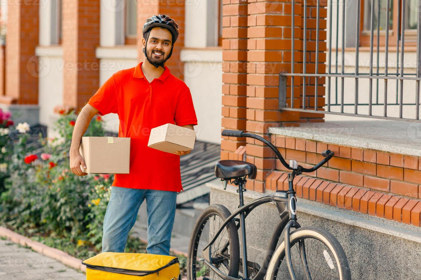 Fast delivery for many online purchases. Smiling courier with beard holds cardboard boxes, near bike and house on street, panorama, copy space photo