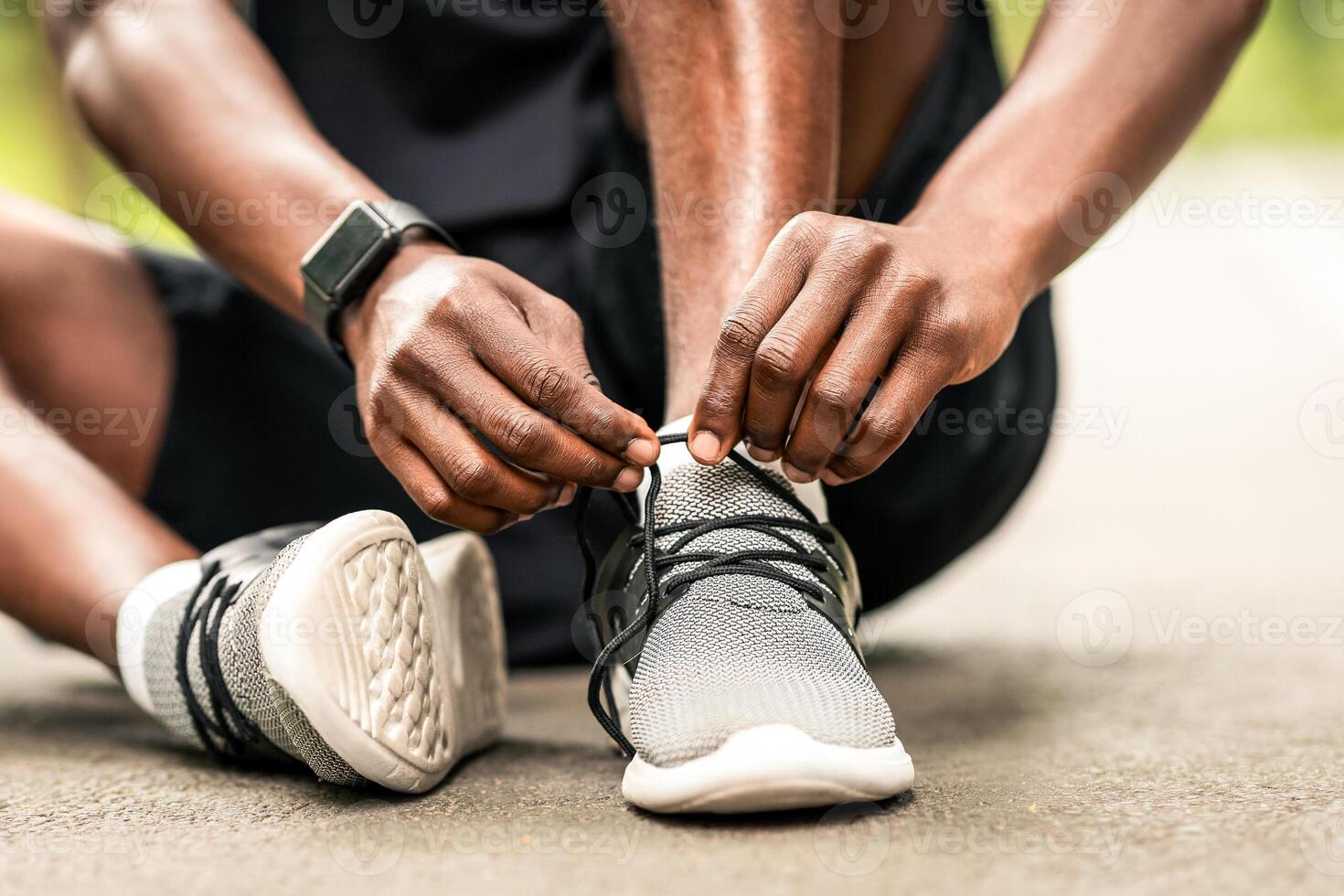 Sportwear concept. Closeup of unrecognizable black sportsman tying his shoelaces before training, sitting on path photo