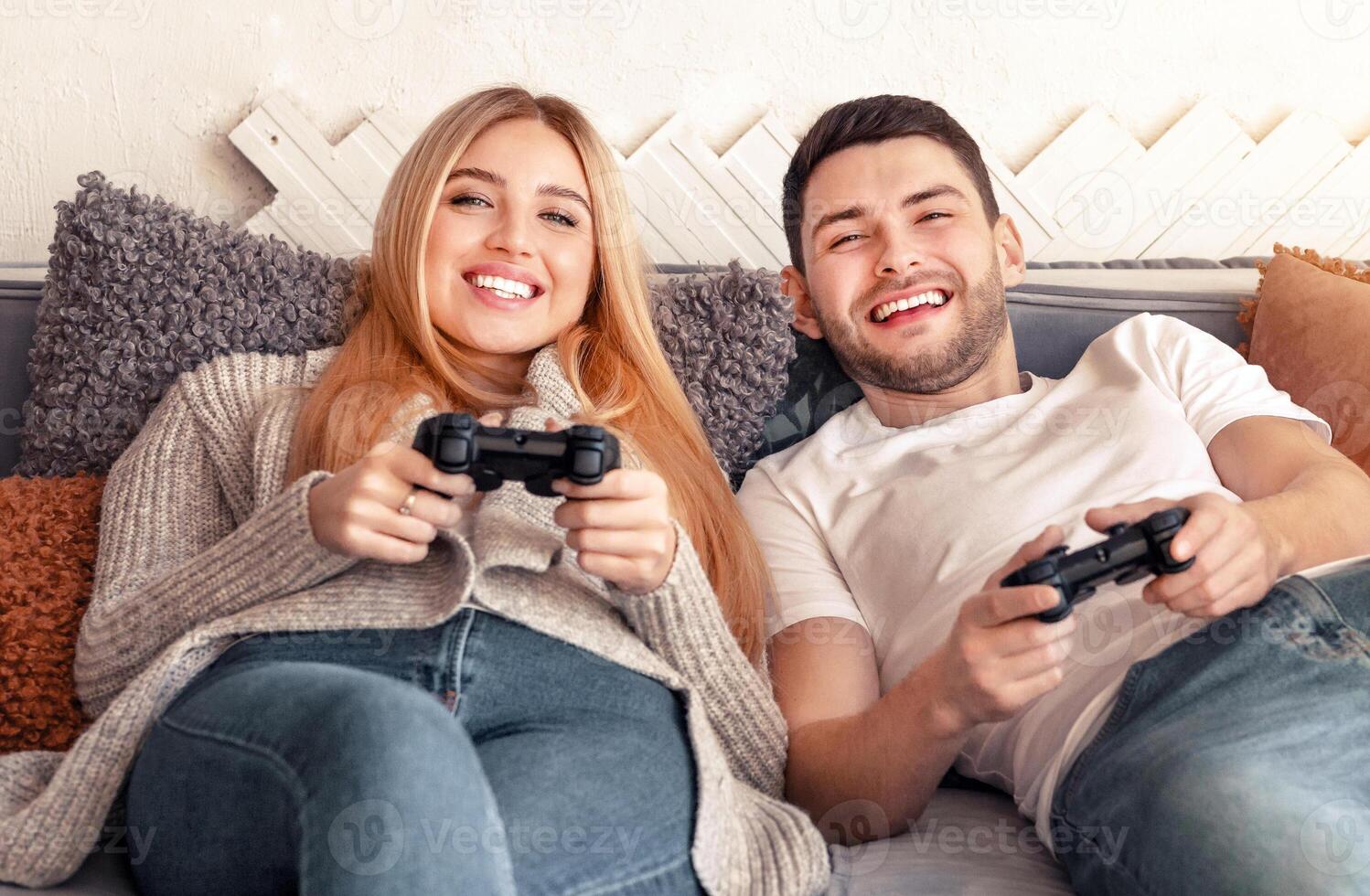 A couple relaxes on a comfortable couch, joyfully playing games together on a relaxing evening. They share laughter and excitement while holding game controllers. photo