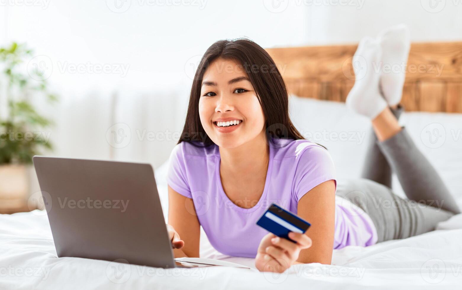 Online Shopping. Chinese Girl Holding Credit Card Using Laptop Purchasing And Buying Things On Internet At Home, Smiling To Camera photo