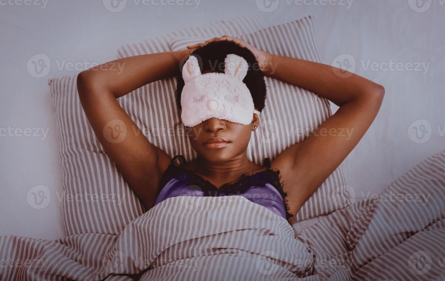 Cozy bed at night, sweet dream, rest at home and healthy lifestyle. Millennial african american female with funny mask, sleeping on bed in interior of bedroom, dark, top view, panorama, empty space photo