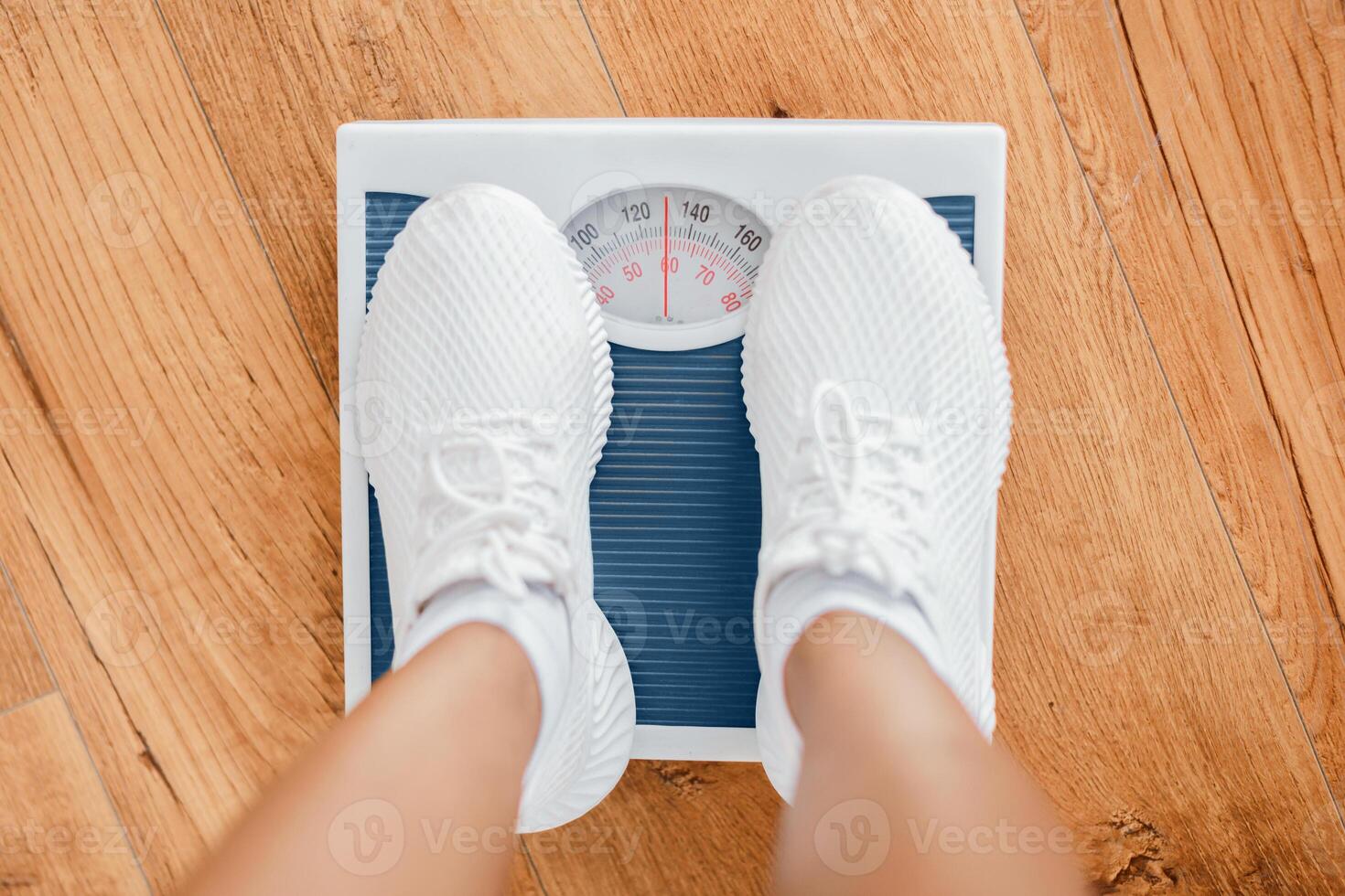 A young African American woman stands on a scale, monitoring her weight as part of her home fitness routine. This scene reflects her commitment to a healthy lifestyle through regular exercise. photo